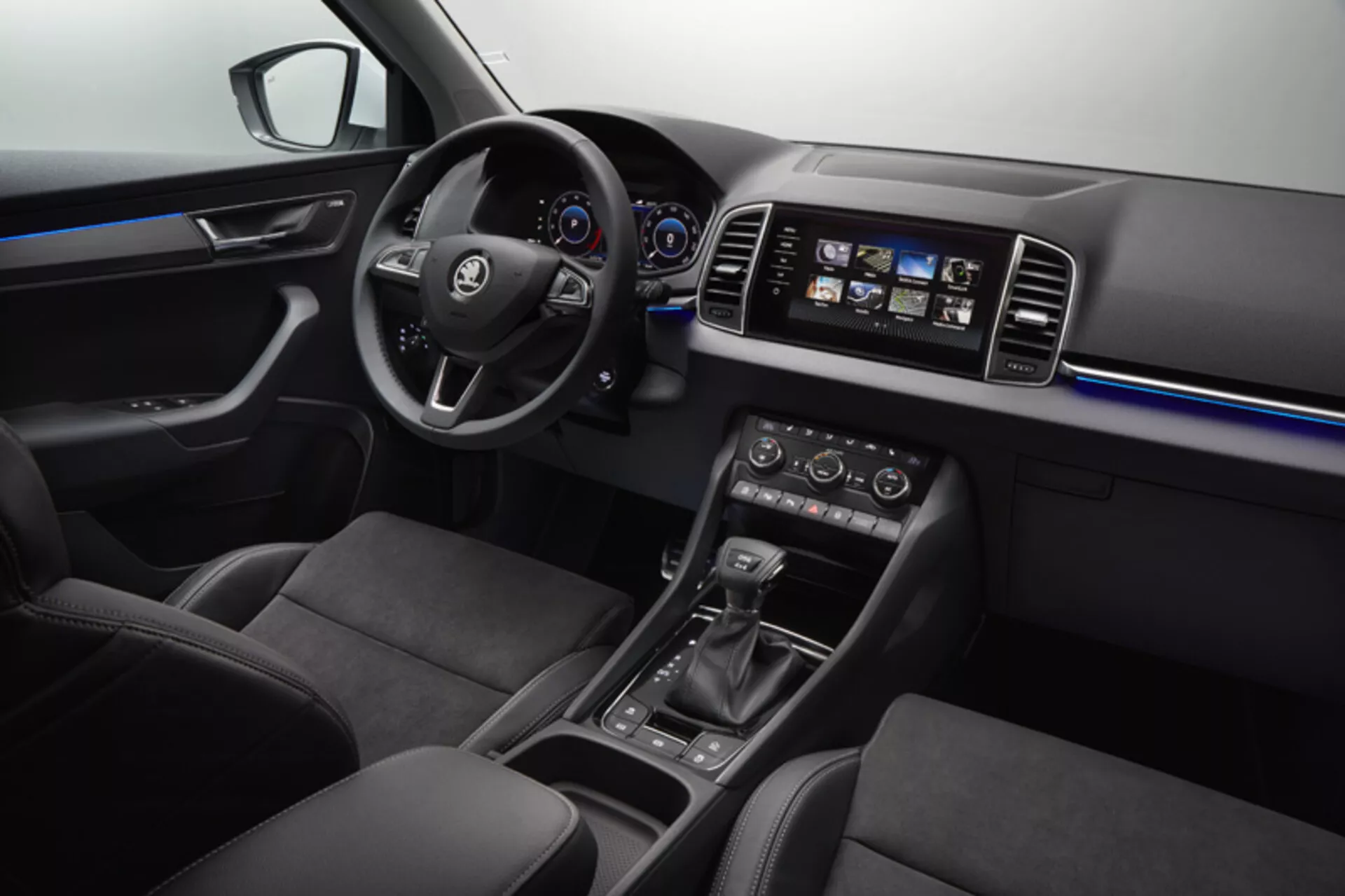 Interiér Škoda Karoq 2017 s volantem s ovládacími prvky, digitálním přístrojovým panelem, prvky středové konzoly, dotykovým informačně-zábavním systémem, klimatizací s dvojitým ovládáním zóny, ambientním vnitřním osvětlením, sportovními předními sedadly a elegantním provedením kombinujícím měkké plasty, akcenty z kartáčovaného kovu a vysokolesklé panely