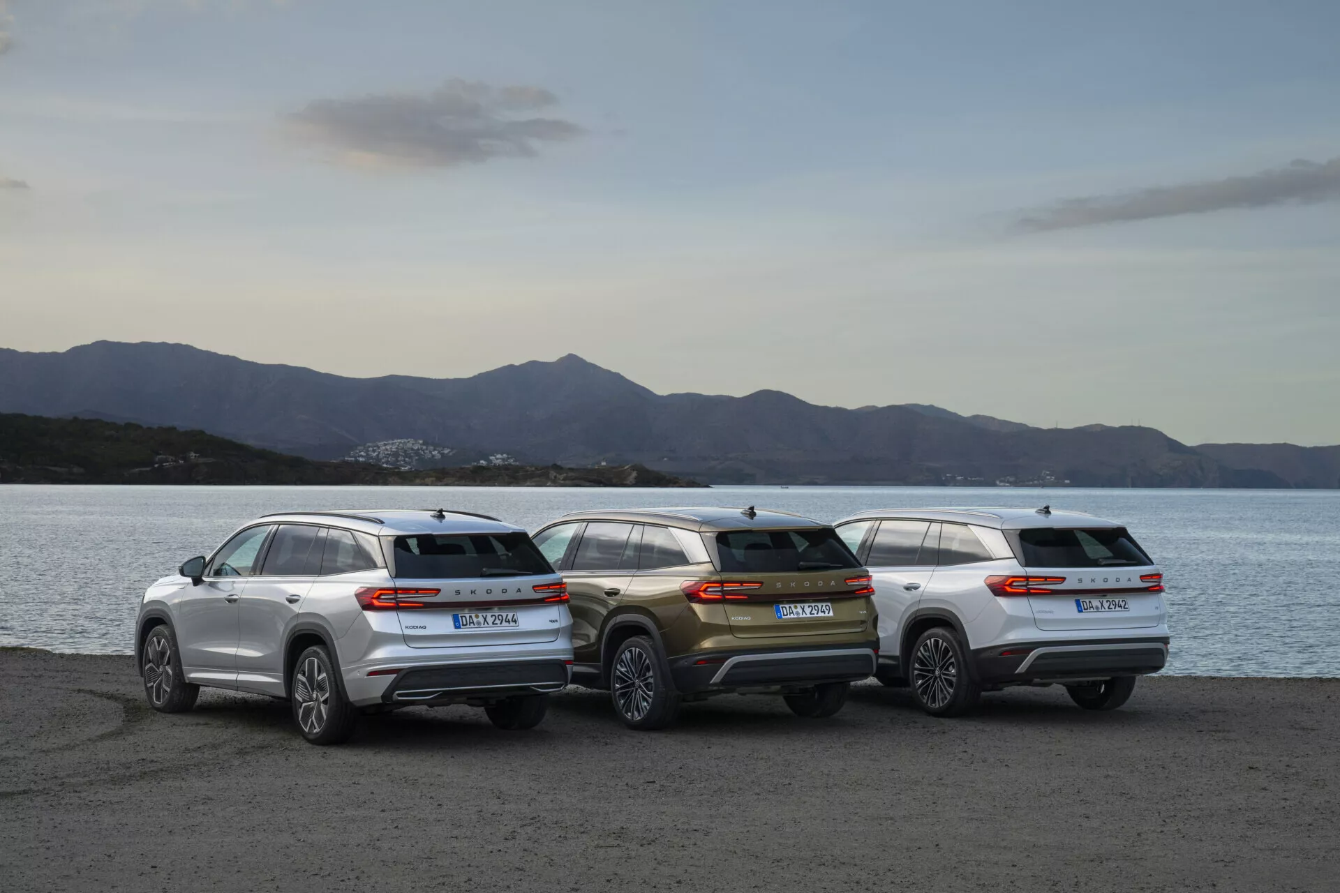Řada SUV Skoda Kodiaq 2024 zaparkovaná na nábřeží během soumraku, prezentující zadní profily a designovou estetiku na pozadí jemně osvětlené krajiny