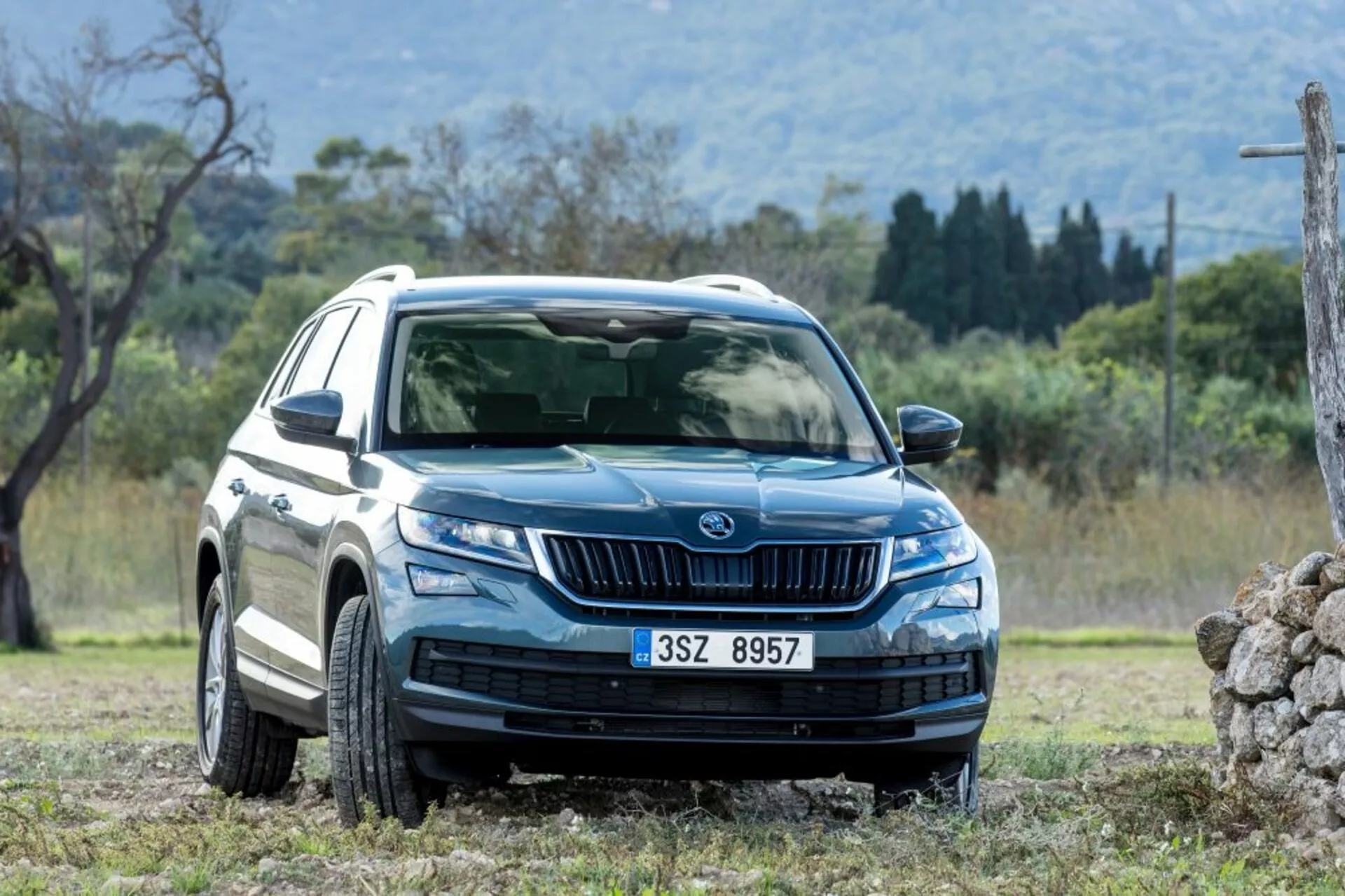 Skoda Kodiaq z roku 2017 v dynamickém úhlu zepředu a zboku ukazuje LED světlomety, denní svícení, přední mřížku s vertikálními lamelami, kola z lehké slitiny s mnoha paprsky, ochranné lemy a obložení karoserie, zrcátka se směrovými signály a tónovaná okna, ve vhodném přírodním prostředí pro jízdu v terénu