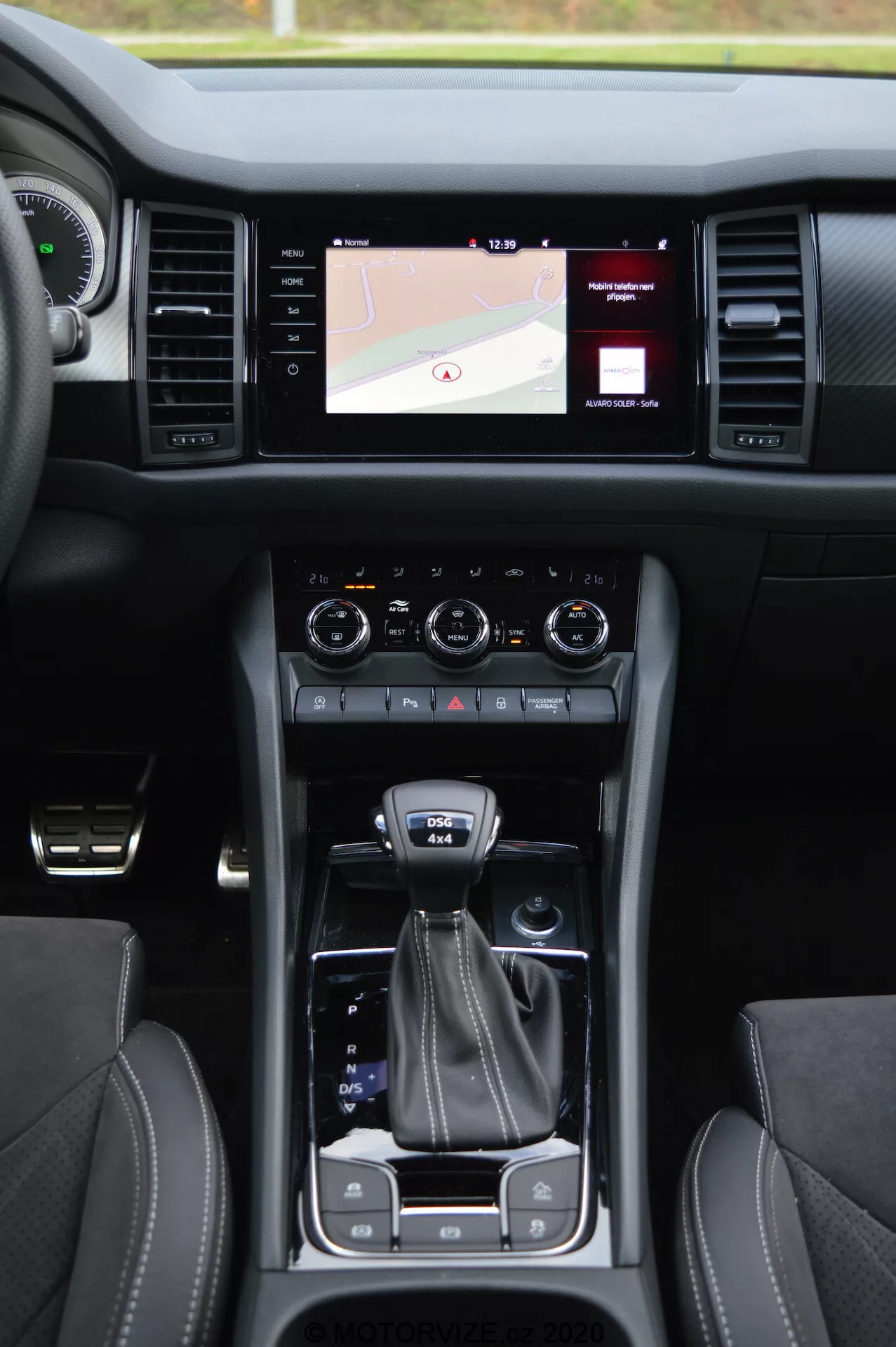 Interiér vozu Skoda Kodiaq 2017 s centrální konzolí, dotykovým informačním systémem zobrazujícím mapu, dvojitými otočnými ovladači klimatizace, voličem jízdních režimů, držáky na nápoje, koženými sedadly s kontrastním prošíváním a tlačítkem bezklíčkového startu