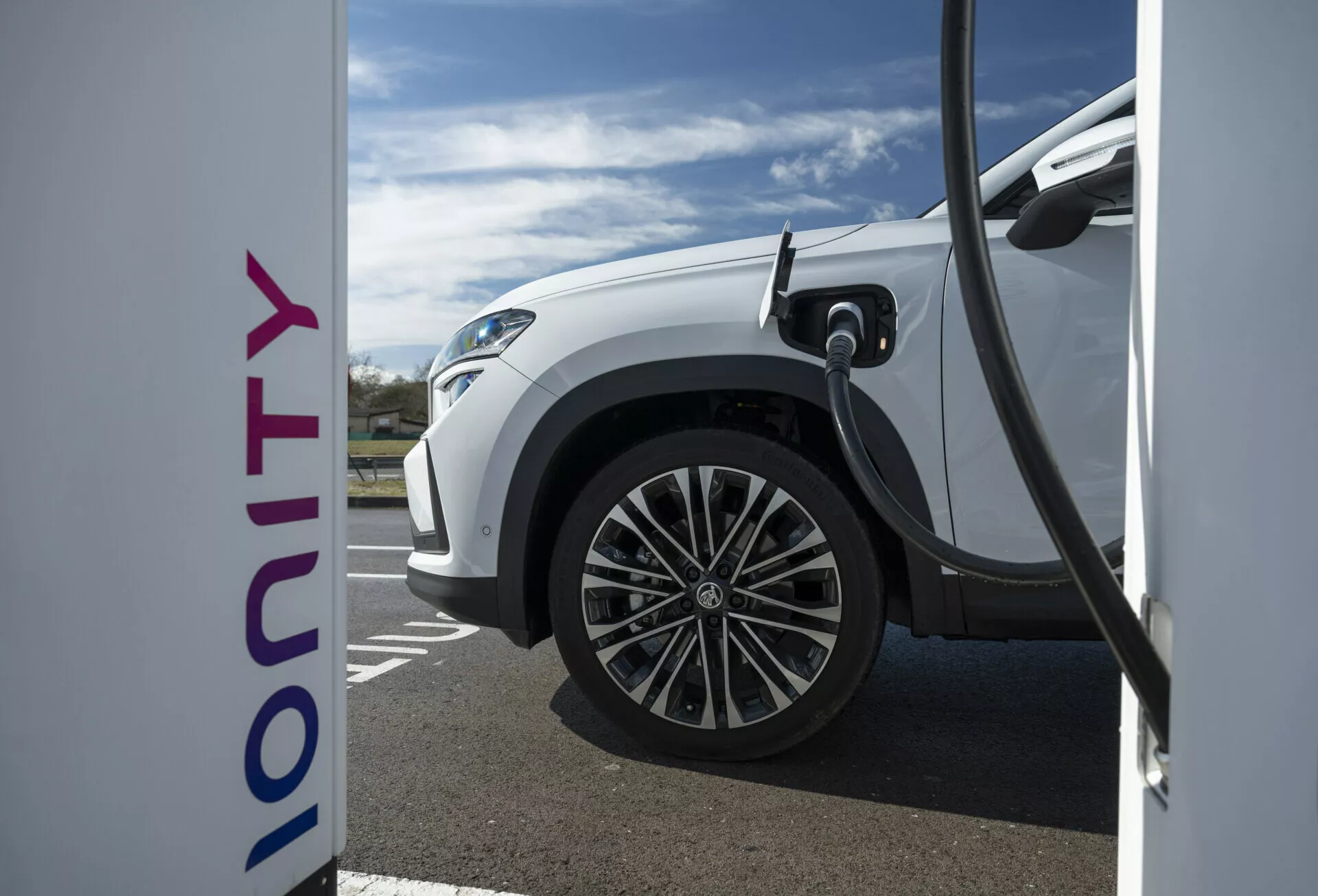 Detailní boční pohled na bílé elektrické vozidlo Škoda Kodiaq 2024 nabíjející na stanici Ionity, představující technologii rychlého nabíjení a moderní design