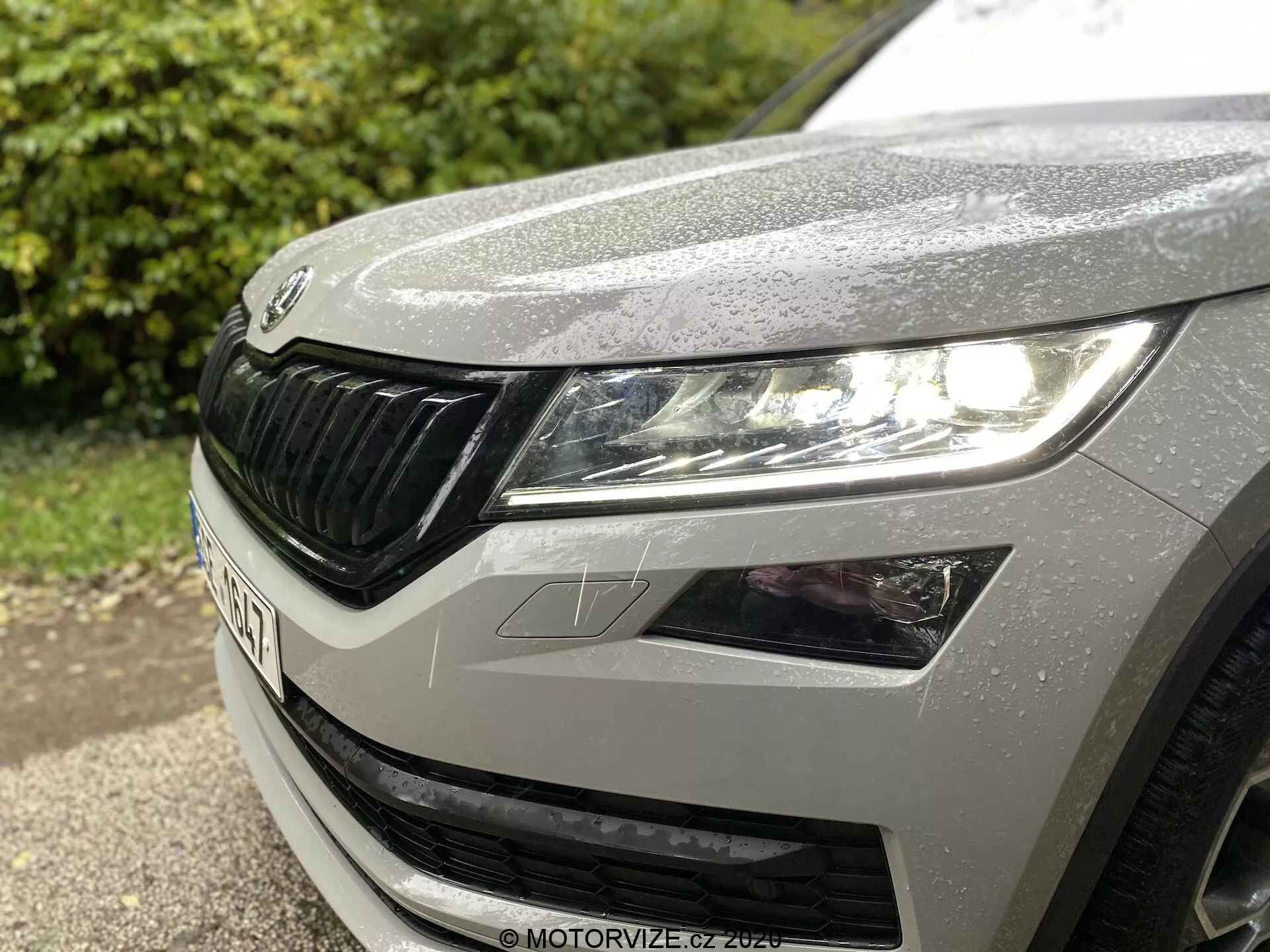 Detailní pohled na levý přední čtvrťák Škoda Kodiaq z roku 2017, zobrazující levý světlomet s moderním LED designem, část kapoty s dešťovými kapkami a charakteristickou mřížkou Škoda s horizontálními prvky.