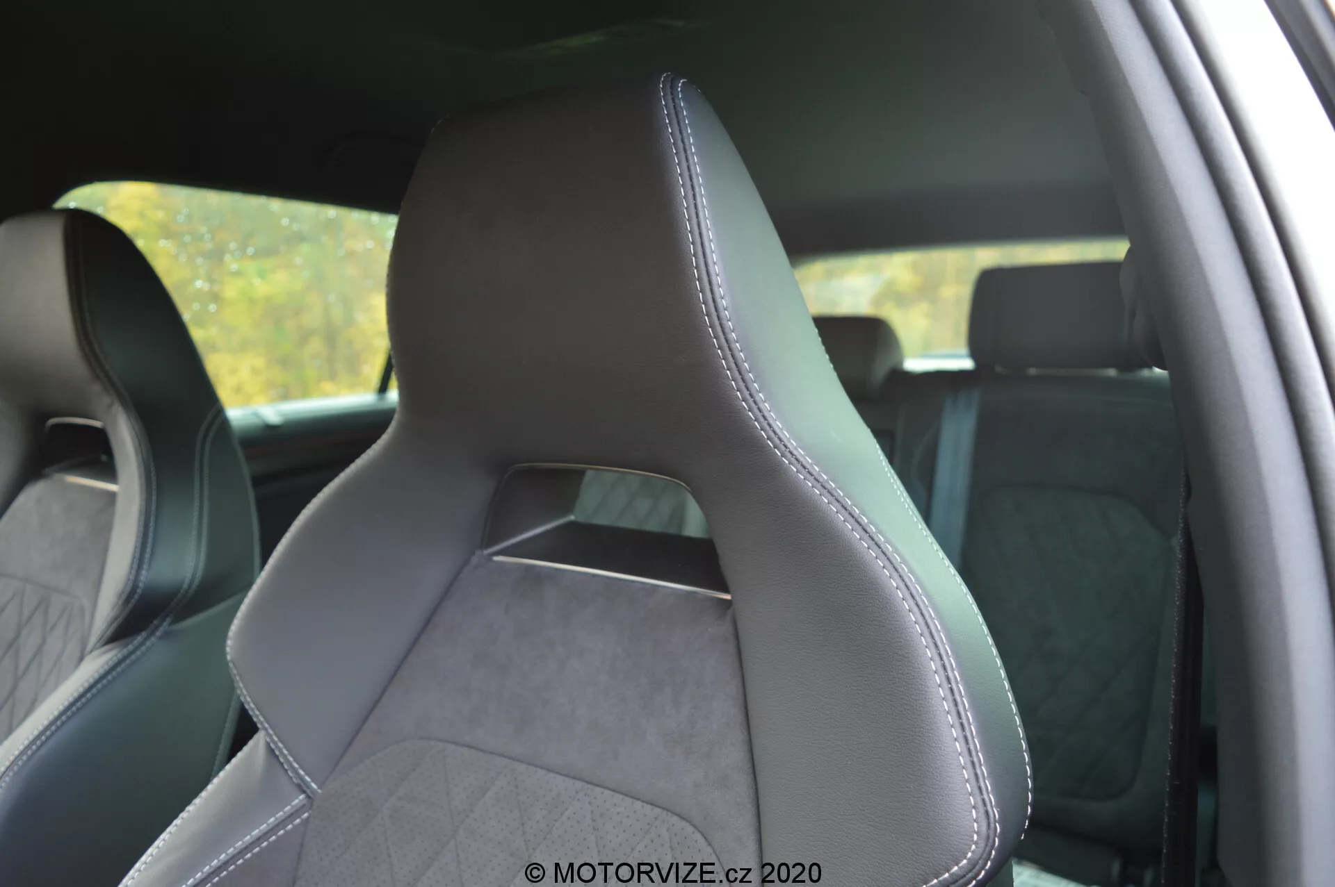 Interiér Škoda Kodiaq 2017 se zaměřením na přední sedadlo řidiče z pohledu zezadu z boku, zdůrazňující čalounění z kůže a texturované tkaniny s přesným prošitím podél okrajů. Moderní, sportovní design sedadla má výrazné boční opěrky pro lepší podporu, integrovanou opěrku hlavy a diamantový šitý vzor naznačující prémiový estetický vzhled. Pozadí interiéru je mírně rozostřené, aby se zdůraznilo sedadlo.