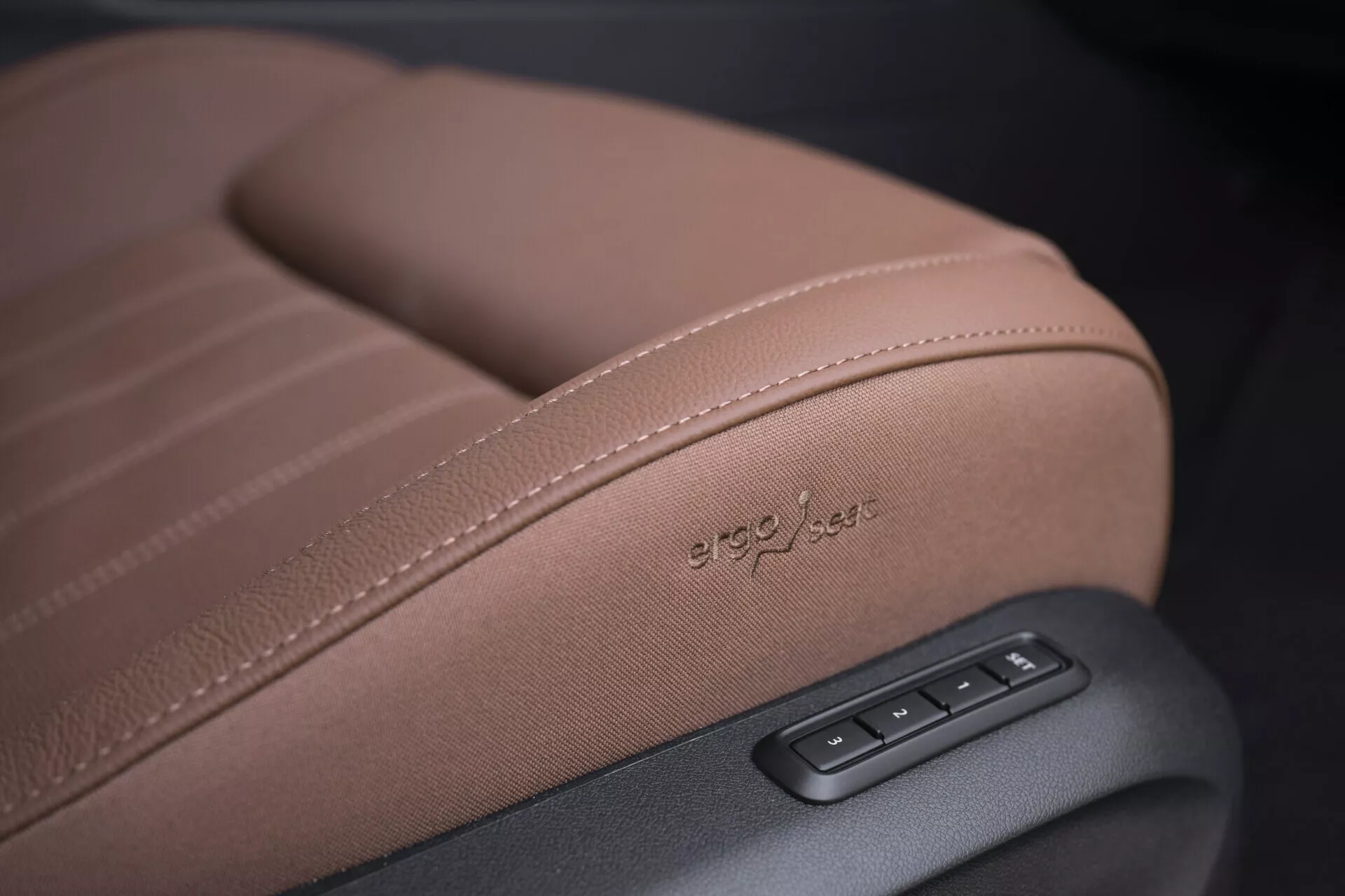 Detailní pohled na sedadlo Škoda Superb 2024 Combi s důrazem na detailní šití, 'ergo-jets' reliéf na čalounění a elektronické ovládání v kvalitní hnědé kůži