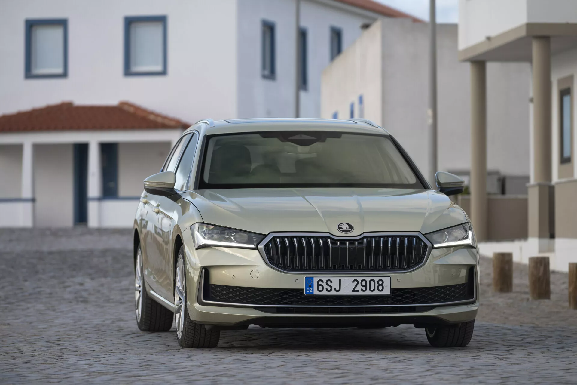 Sedan Škoda Superb Combi 2024 v dynamickém tříčtvrtečním pohledu prezentující LED světlomety a sportovní slitinová kola na dlažební ulici v teplém slunečním světle