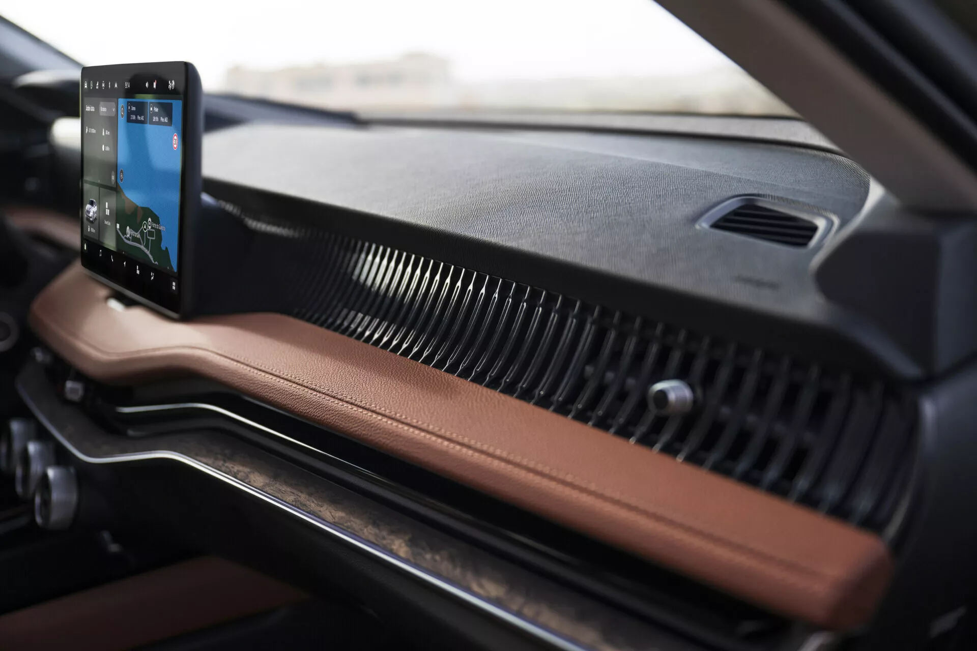 Blízký pohled na interiér palubní desky automobilu Skoda Superb 2024 s vertikálně orientovaným dotykovým infotainment systémem s integrovanou navigací, koženými a plastovými materiály a moderními horizontálními větracími mřížkami.