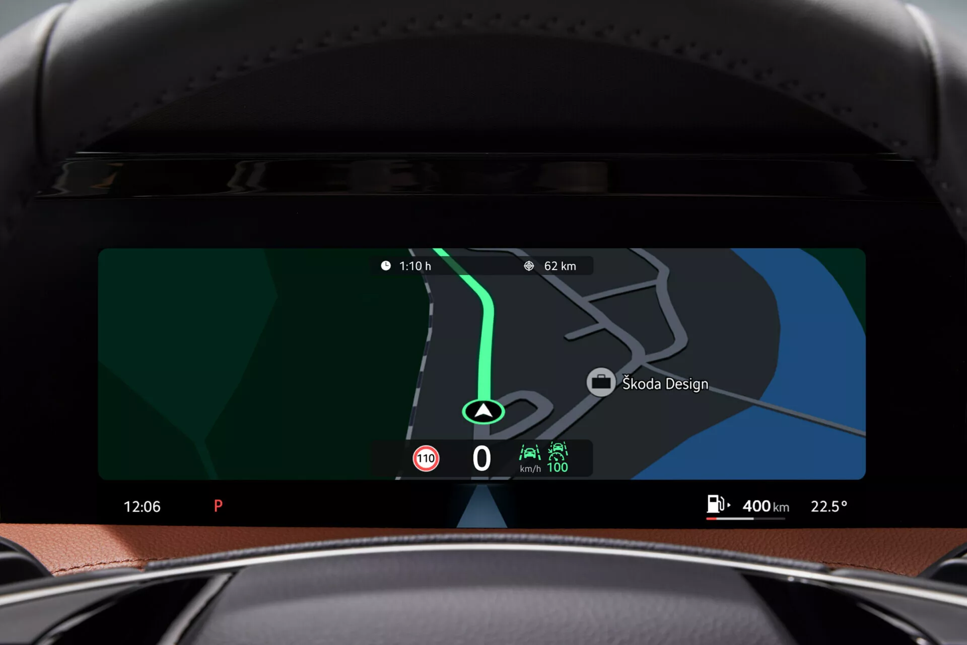 Pohled na interiér vozu Škoda Superb Limousine 2024 ukazující pokročilý digitální displej, jak je viděn z pohledu řidiče. Přístrojová deska má širokou vodorovnou obrazovku zobrazující navigační mapu s ukazateli vzdálenosti (110 m, 6.2 km), štítek Škoda Design, aktuální čas (12:06), indikátor režimu parkování (P), teplotu (22.5°) a rychloměr na 0 km/h. Další ikony naznačují možnosti konektivity a asistenční funkce řidiče. Viditelná je i horní část elegantního, černého volantu oproti minimalistické přístrojové desce bez tlačítek.