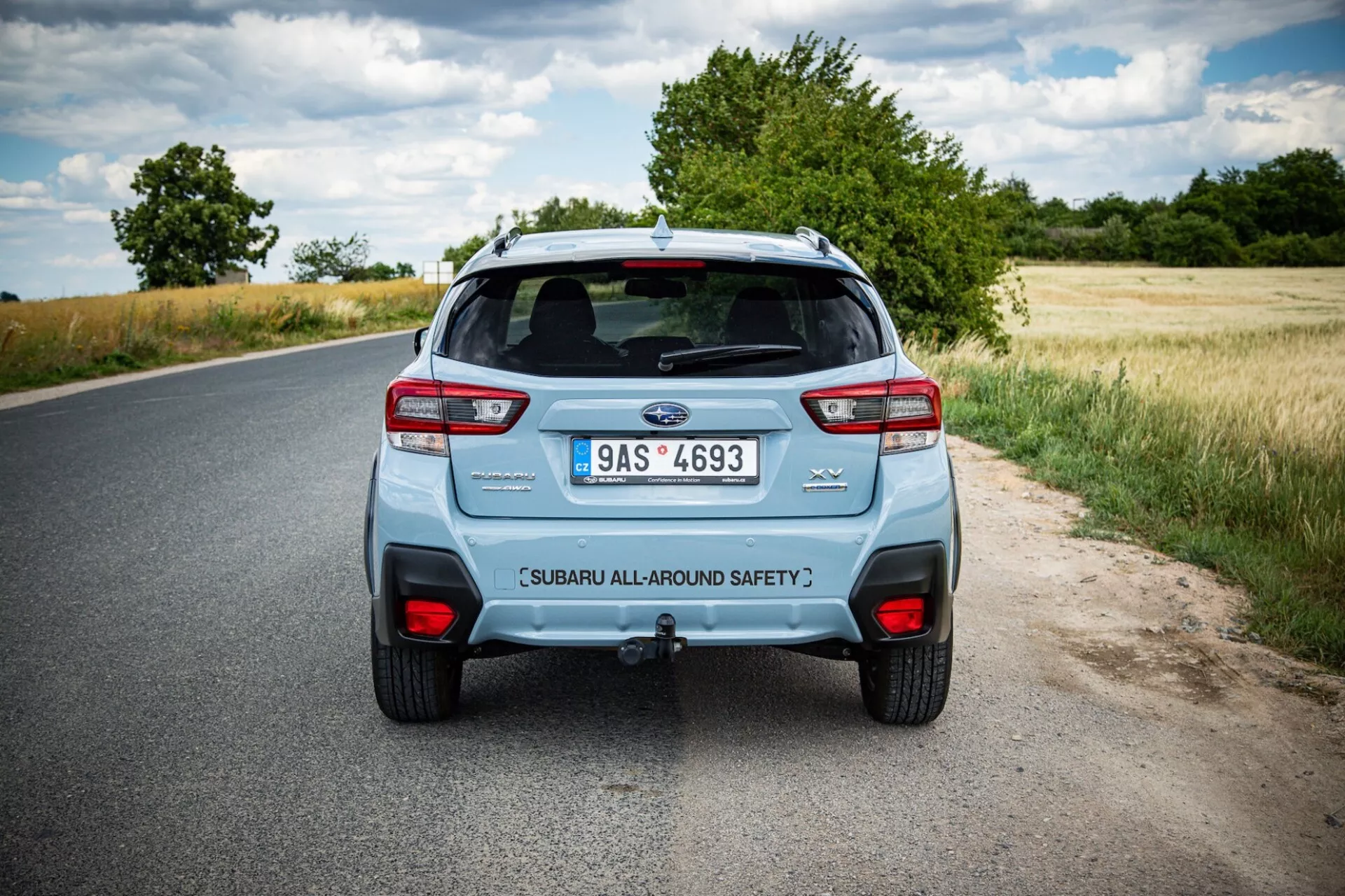 Zadní pohled na Subaru XV 2021 na venkovské silnici, ukazuje charakteristická zadní světla, dvojitý výfukový systém a zvedací vrátka s bezpečnostním označením pod částečně zataženou oblohou