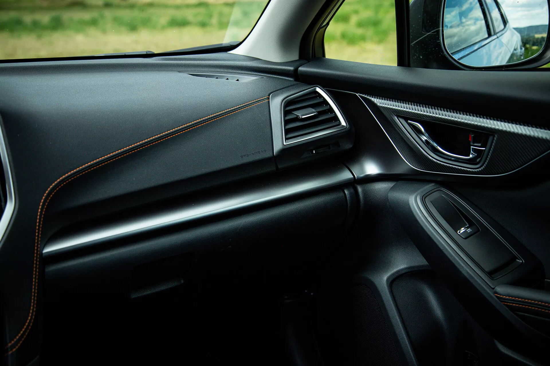 Interiér Subaru XV 2021 s pohledem na stranu spolujezdce ukazující elegantní design palubní desky s kontrastním prošíváním, ergonomickou kličku dveří s ovládáním, integrovaný reproduktor, vzduchové otvory zdobené chromem a ambientní osvětlení