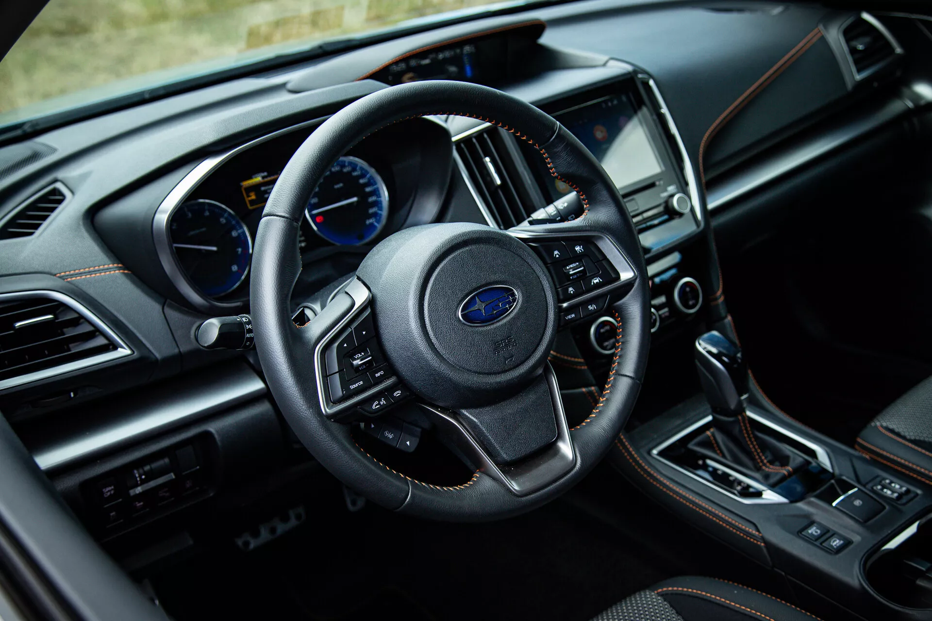 Interiér Subaru XV 2021 z pohledu řidiče s koženým volantem se zabudovanými ovladači, analogovým a digitálním přístrojovým panelem, dotykovým informačním systémem a automatickou převodovkou