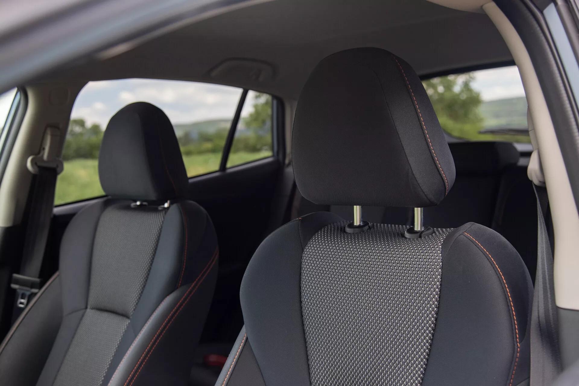 Interiérový pohled na Subaru XV 2021 s černými koženými sedadly s vložkami z vzorované látky a charakteristickým oranžovým prošíváním, zaměřený na pohodlí a design z perspektivy zadního pasažéra