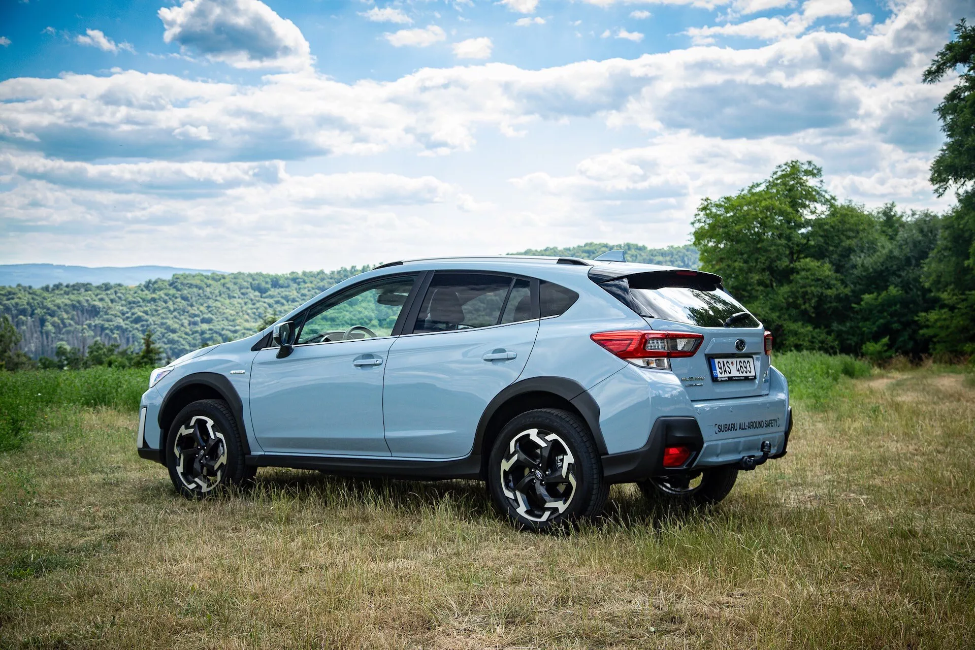 Světle zabarvené SUV fotografované z tříčtvrtečního zadního úhlu, které ukazuje boční a zadní design s vícepaprskovými slitinovými koly, tónovanými okny a potenciálními technickými funkcemi, parkované v přírodním prostředí