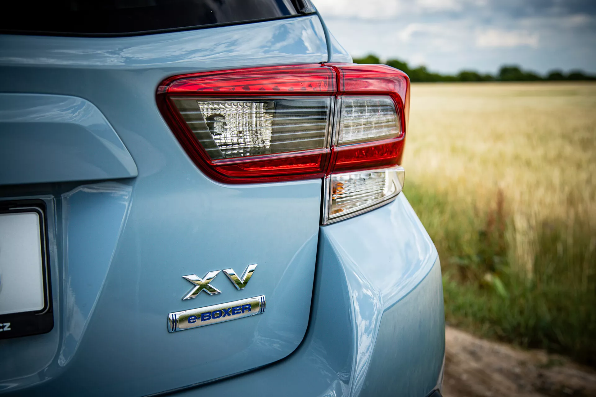 Detailní pohled na zadní levou stranu Subaru XV 2021 s emblémem hybridního pohonu e-BOXER a podrobně zpracovaným světlem zadního světla na metalickém světle modrém laku v venkovském prostředí