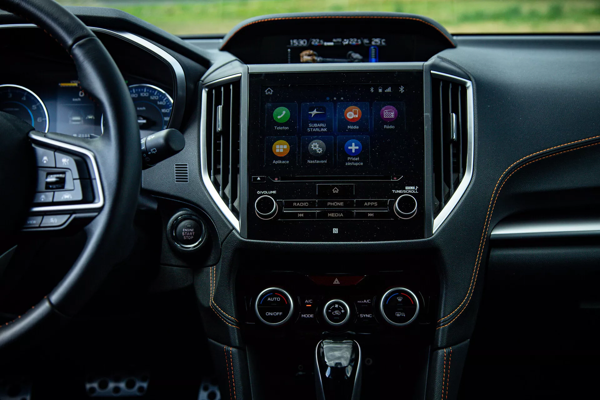 Interiér Subaru XV 2021 s důrazem na středovou konzoli a multimediální systém z pohledu ze zadního sedadla, zobrazující dotykovou obrazovku s ikonami aplikací, tlačítka pro ovládání audia a klimatizace, odrážející pokročilou technologii a luxusní design