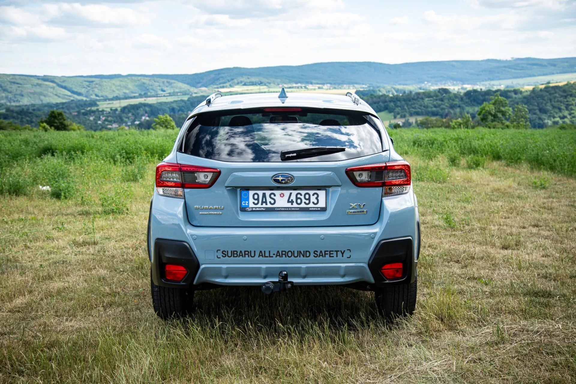 Zadní úhel Subaru XV 2021 venku na poli s kopcím na pozadí, zdůrazňuje bezpečnostní prvky a moderní designové prvky SUV, jako je zadní spoiler a výrazná zadní světla