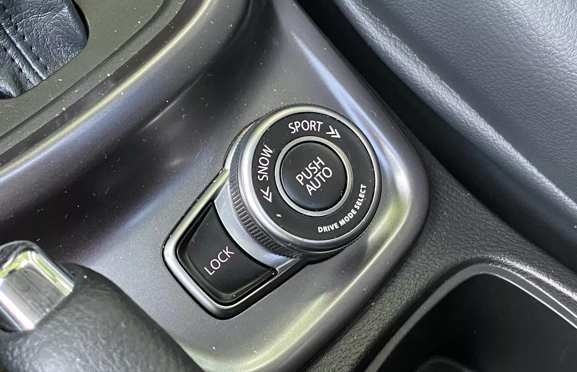 Detailní záběr voliče jízdních režimů umístěného v centrální konzoli Suzuki Vitara 2018, obsahující popisky pro režimy SNOW, SPORT, LOCK a AUTO, texturovaný obvod a kartáčované kovové akcenty.