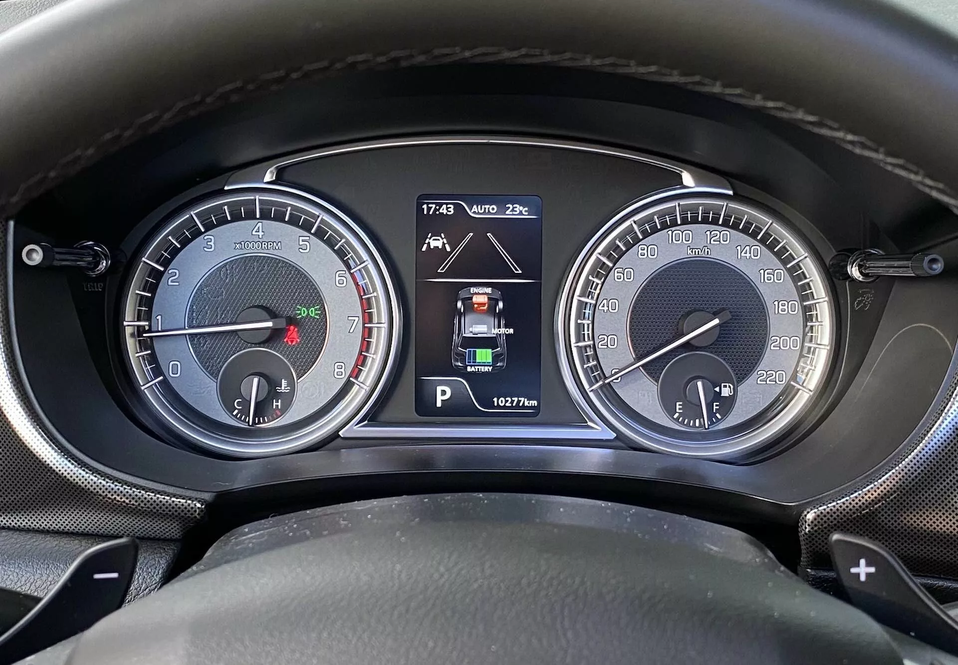 Detailní záběr na přístrojovou desku/ovládací panel Suzuki Vitara 2018 z pohledu řidiče. Obrázek obsahuje dva analogové ciferníky, včetně otáčkoměru (do 7000 rpm) s malým ukazatelem paliva a rychloměru (do 260 km/h) s malým ukazatelem teploty motoru. Centrální digitální displej ukazuje režim Park, indikátory parkovacích asistentů, teplotu okolí (20°C), čas (17:43) a počet najetých kilometrů (162776 km). Označení pádel řazení napovídá na automatickou nebo poloautomatickou převodovku.