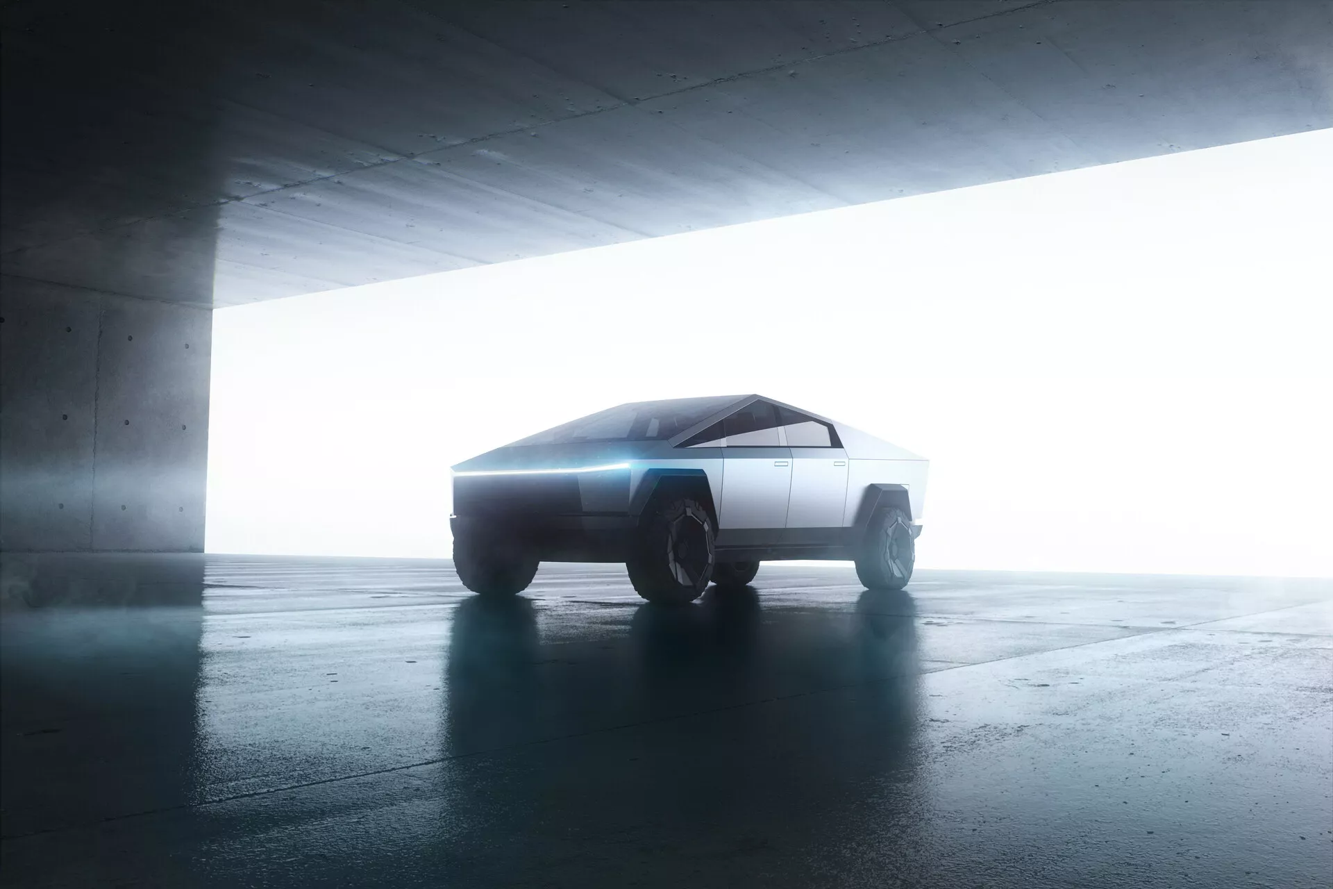 Boční pohled na Tesla Cybertruck 2021 v parkovací garáži. Vozidlo s futuristickým, hranatým designem je mírně natočeno směrem k fotoaparátu a ukazuje své minimalistické, geometrické linie. Protisvětlo zvýrazňuje siluetu a vytváří efekt halo. Ostré, ploché povrchy a robustní off-road kola naznačují pokročilou, pravděpodobně elektrickou pohonnou technologii.