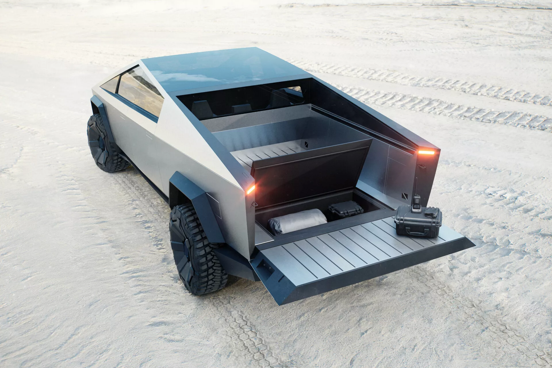 Futuristický Tesla Cybertruck 2021 (1. generace) zaparkovaný na písečném povrchu, zachycený z vyvýšeného zadního tříčtvrtního pohledu. Úhlový, polygonální design s plochou korbou a motorizovaným víkem sklopeným dolů, které odhaluje vestavěnou rampu. Vozidlo také obsahuje uzamykatelnou tonneau kryt, velké off-road pneumatiky a matně šedý povrch, který přispívá k minimalistické, průmyslové estetice. Žádné tradiční kliky dveří ani boční zrcátka nejsou viditelné, což naznačuje výsuvné kliky a zrcátka založená na kamerách. Spekulovaně je elektrické, zaměřené na praktičnost a schopnost jízdy v terénu.