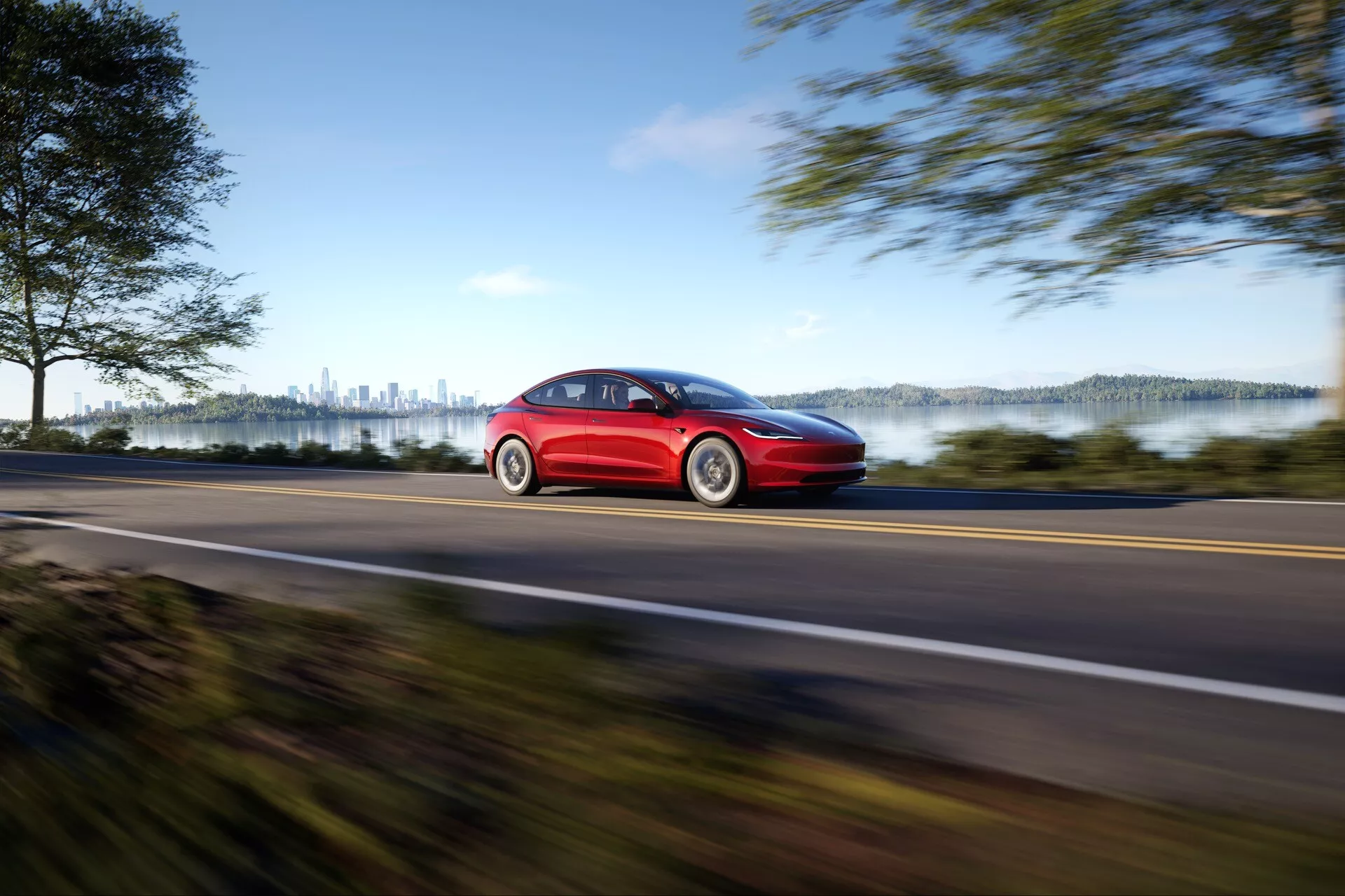 Červený Tesla Model 3 (1. generace po faceliftu) z roku 2023 demonstrující rychlost s rozostřeným efektem na venkovské silnici z profilu