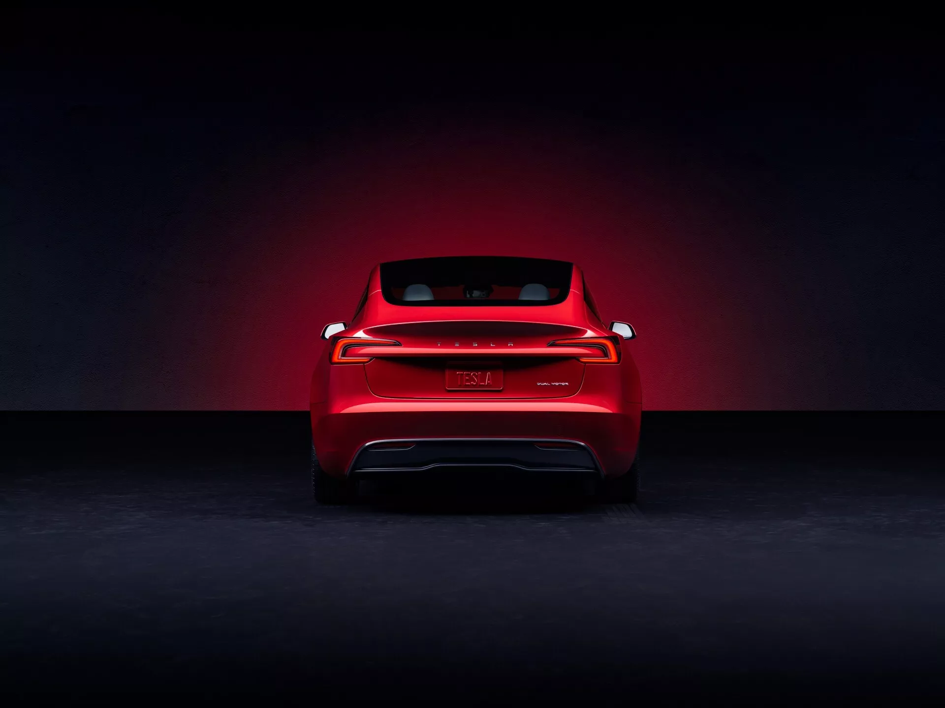 Tesla Model 3 2023 (facelift první generace) prezentovaná z zadního pohledu pro promoční účely ve studiu, s červeným lakem, dramatickým efektem světelného halo, moderními LED zadními světly po celé šířce, znakem bez viditelné značky, náznaky elektrického vozidla bez výfuku a sportovní siluetou zadního okna.