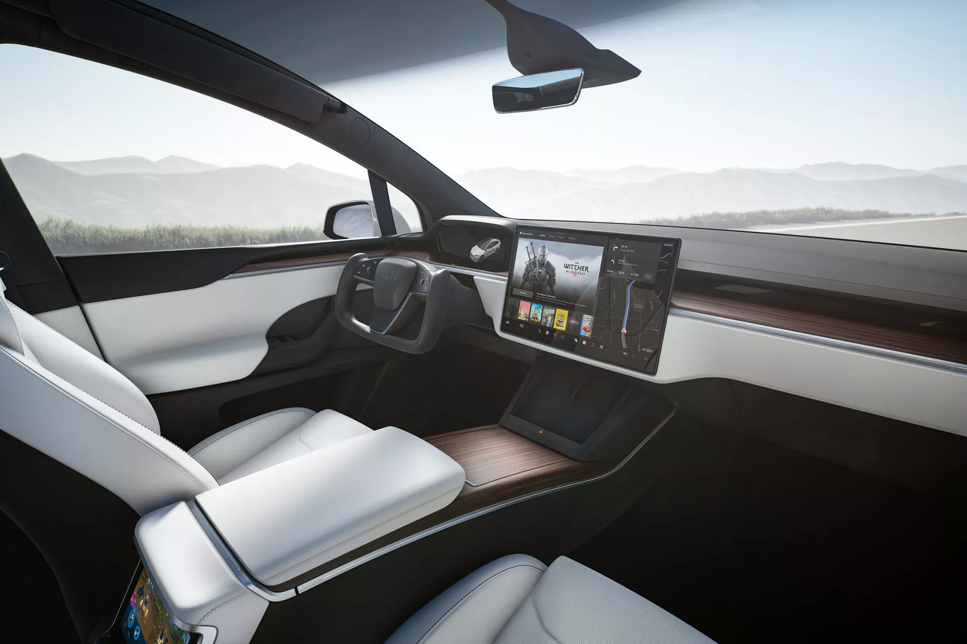 Interiér Tesla Model X 2021, zobrazený z mírně nakloněného úhlu na stranu spolujezdce, s moderní palubní deskou a velkým, uprostřed umístěným dotykovým infotainment systémem s barevnými grafikami. Bílá sedadla spolujezdce kontrastují s tmavší palubní deskou a dřevěnou lištou. Smartphone leží na potenciální bezdrátové nabíjecí podložce na čisté středové konzole a velká přední okna přispívají k vzdušnosti a otevřenému pocitu kabiny. Filigránové zpětné zrcátko na horním středu čelního skla naznačuje pokročilé funkce, jako je automatické ztmavování nebo zobrazení zadní kamery.