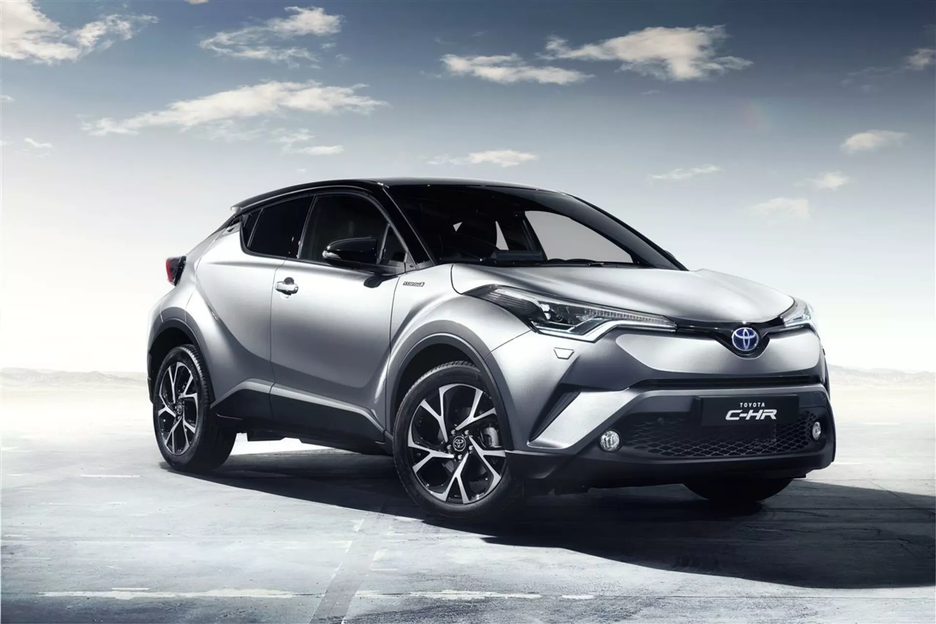 Crossover SUV Toyota C-HR 2016 zobrazený v digitálně renderované otevřené krajině s oblačnou oblohou, který zdůrazňuje jeho vysokou světlou výšku, moderní LED světlomety, sportovní slitinová kola a aerodynamicky tvarovanou karoserii pro lepší výkon a účinnost.