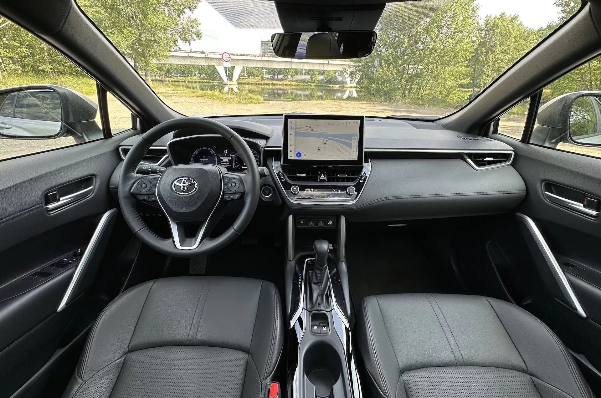 Interiér Toyota Corolla Cross 2022 z pohledu ze zadního sedadla, prezentující palubní desku, dotykový informační systém a přední sedadla potažená kůží