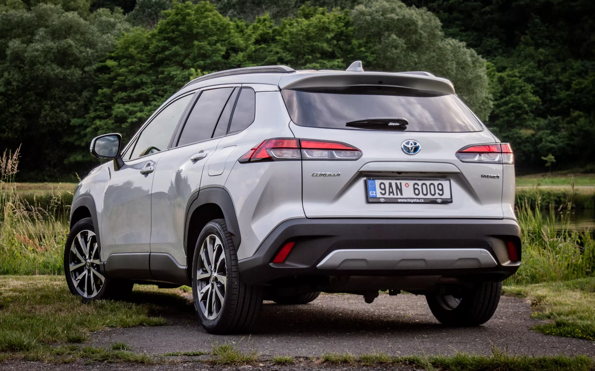 Zadní tříčtvrteční pohled na Toyota Corolla Cross 2022 ukazující LED zadní svítilny, odznak hybridu a senzory parkovací asistence