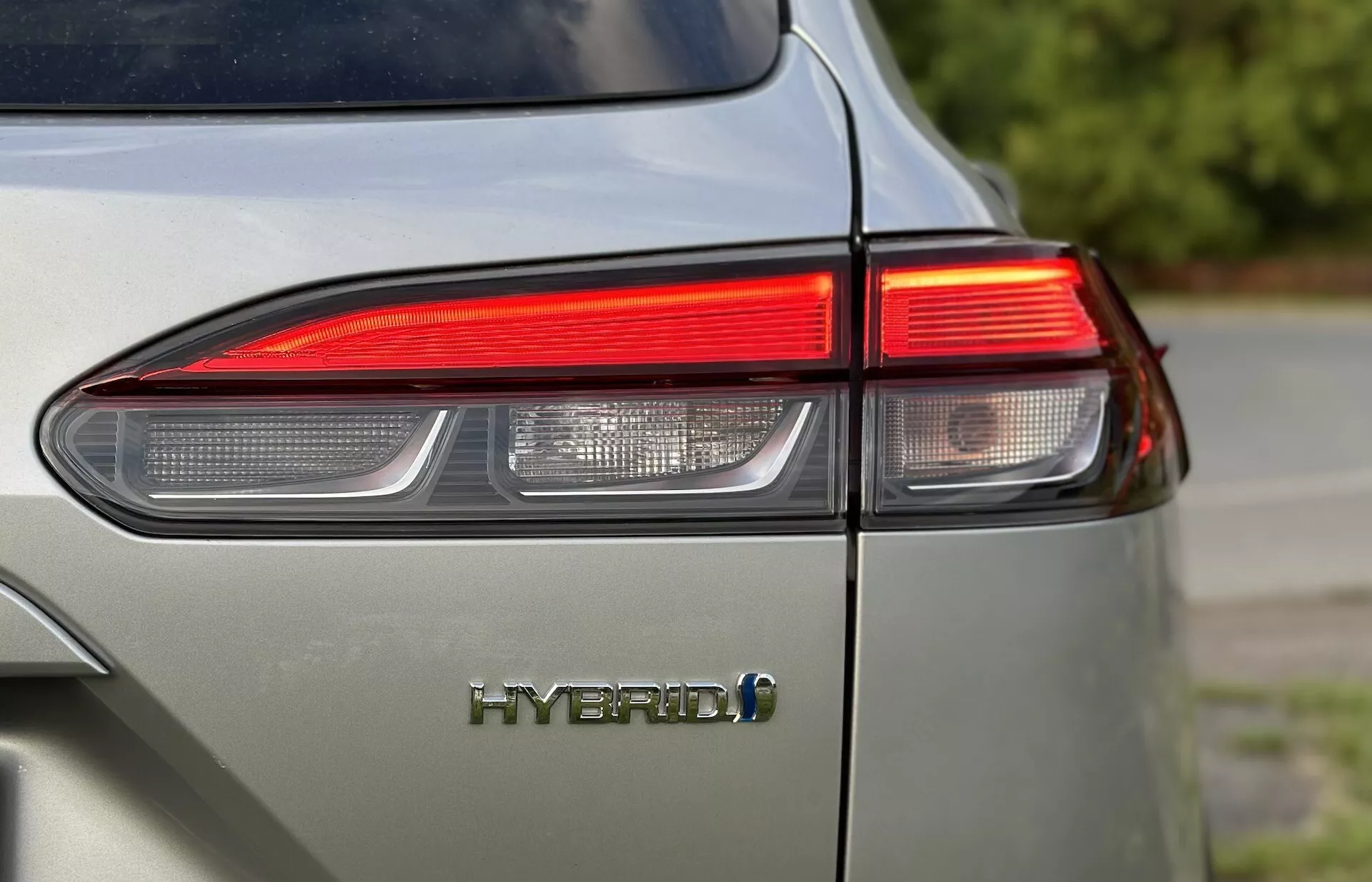 Detailní záběr na zadní levý roh Toyota Corolla-Cross 2022 zobrazující design LED zadního světla a emblém HYBRID se zaměřením na ekologicky šetrnou technologii vozidla a lesklý povrch v tlumené světle šedé barvě
