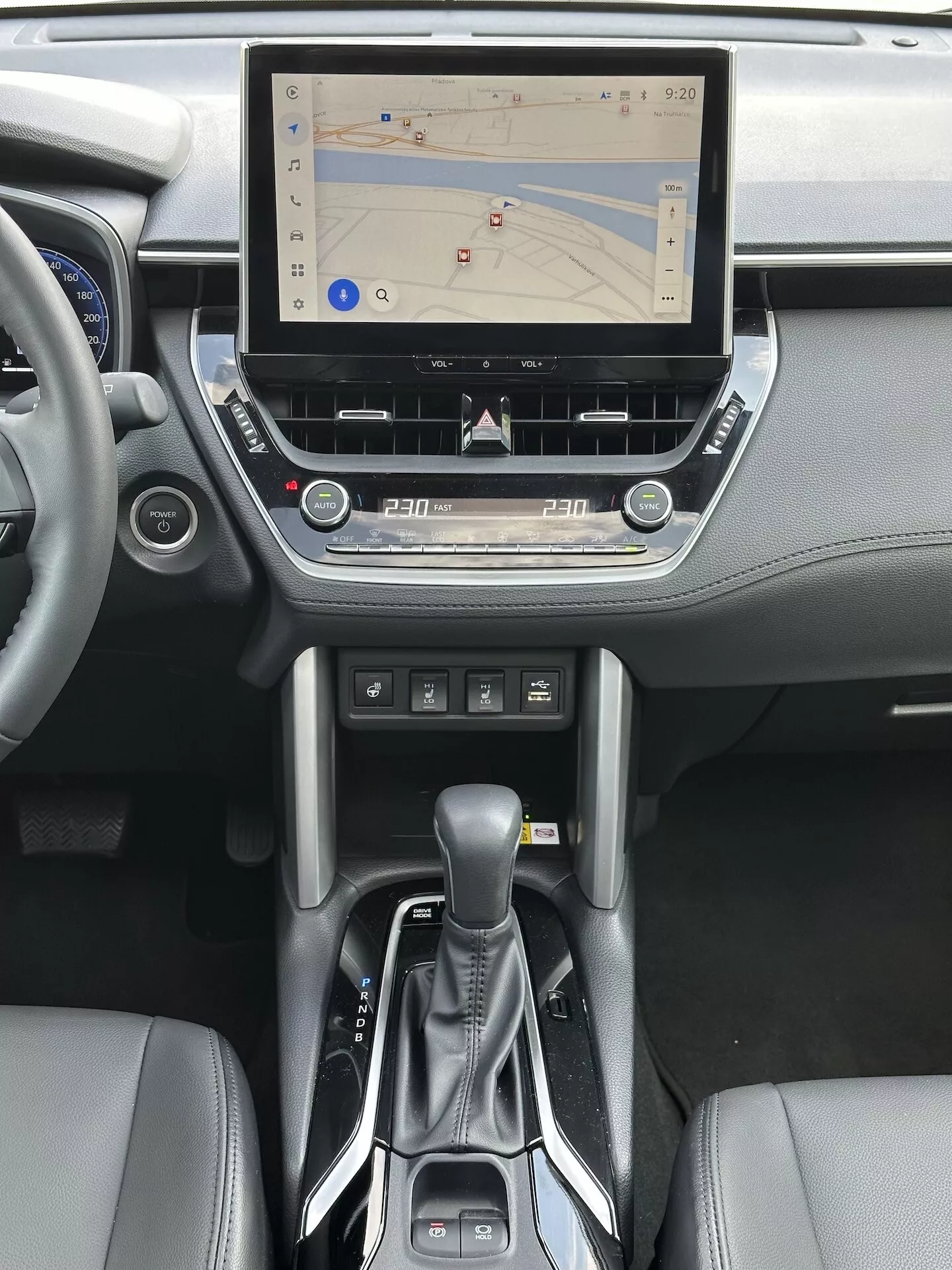 Interiér Toyota Corolla Cross 2022 s dotykovým informačním systémem s GPS navigací, duální klimatizací, slotem pro CD, tlačítky pro ovládání médií a telefonu, moderním voličem automatické převodovky a akcenty z kůže na středové konzoli a designu palubní desky