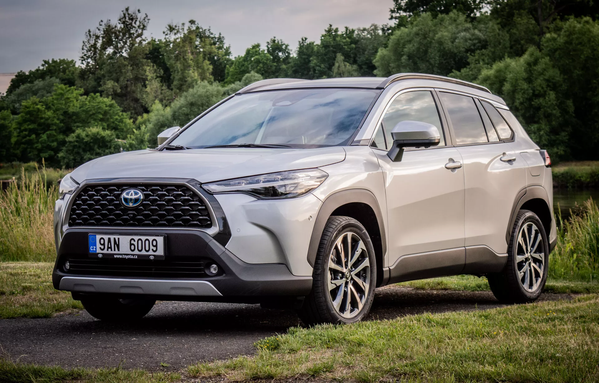 Toyota Corolla Cross 2022 předvádí svůj dynamický design s perspektivou zepředu a ze strany, zvýrazňuje velkou vzorovanou přední mřížku, úzké LED světlomety a vícepaprsková slitinová kola, zaparkovaný v přírodním parku