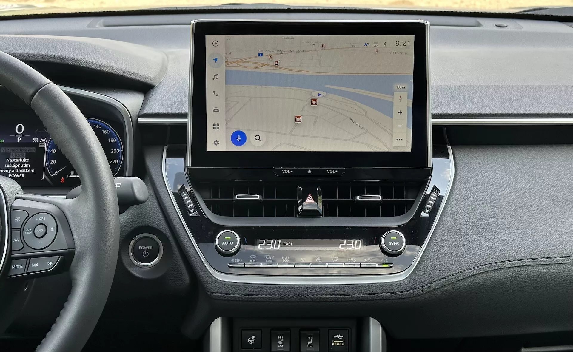Interiér Toyota Corolla Cross 2022 předvádějící moderní středovou konzolu s velkým, vertikálním dotykovým displejem pro navigaci, obklopeným elegantními prvky palubní desky s koženým zdobením, digitálním přístrojovým panelem vedle volantu a ergonomickými taktickými ovladači pro klimatizaci a zvuk, v přirozeném osvětlení.