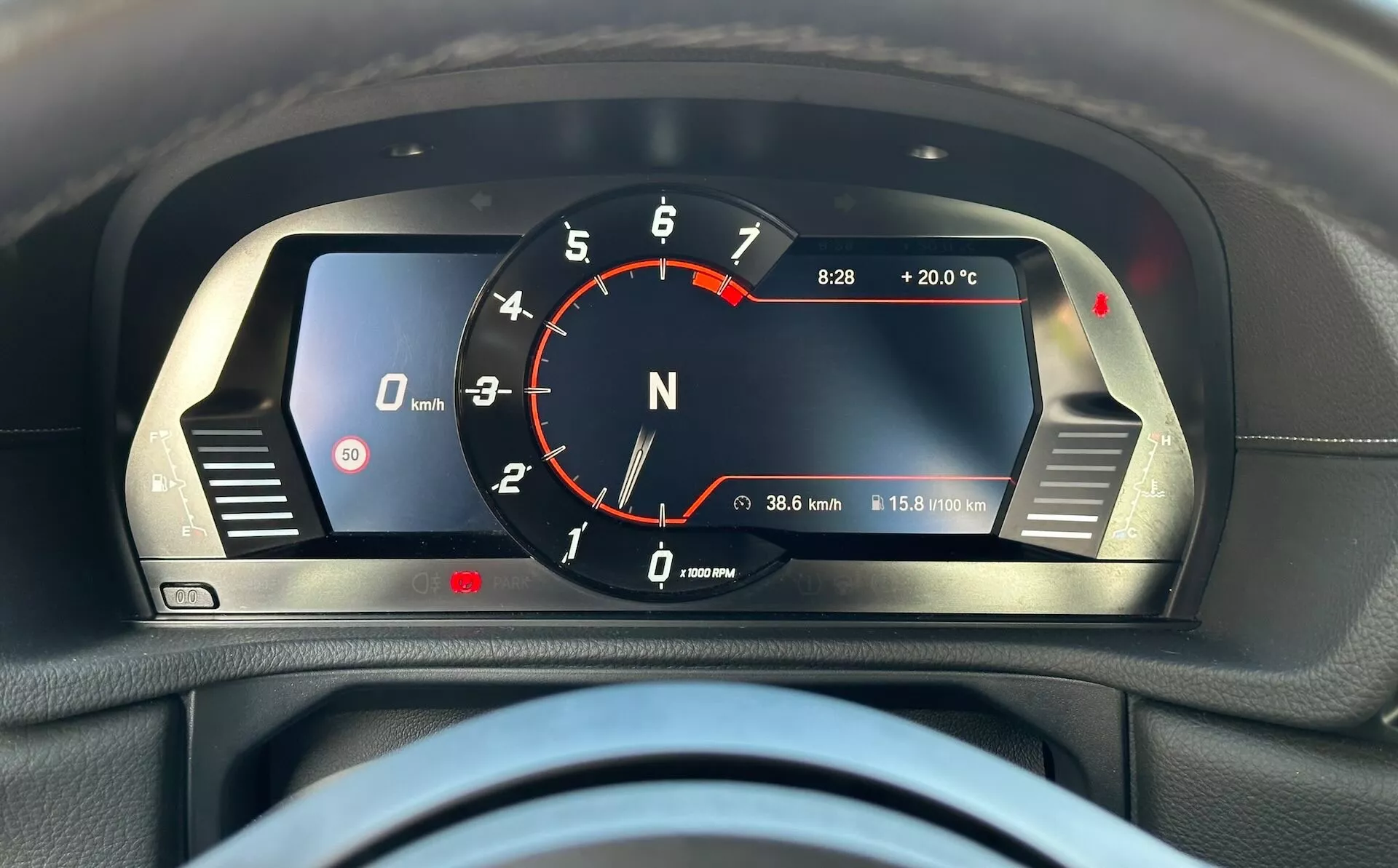 Detailní pohled na digitální přístrojovou desku Toyota GR Supra 2019 s červeným analogovým tachometrem, digitálním rychloměrem, indikátorem neutrálního stupně, digitálním hodinami s vnější teplotou, tachometrem, počítačem ujeté vzdálenosti a varovnými světly, vše umístěné v elegantním černém pouzdře se stříbrnými dekorativními prvky.