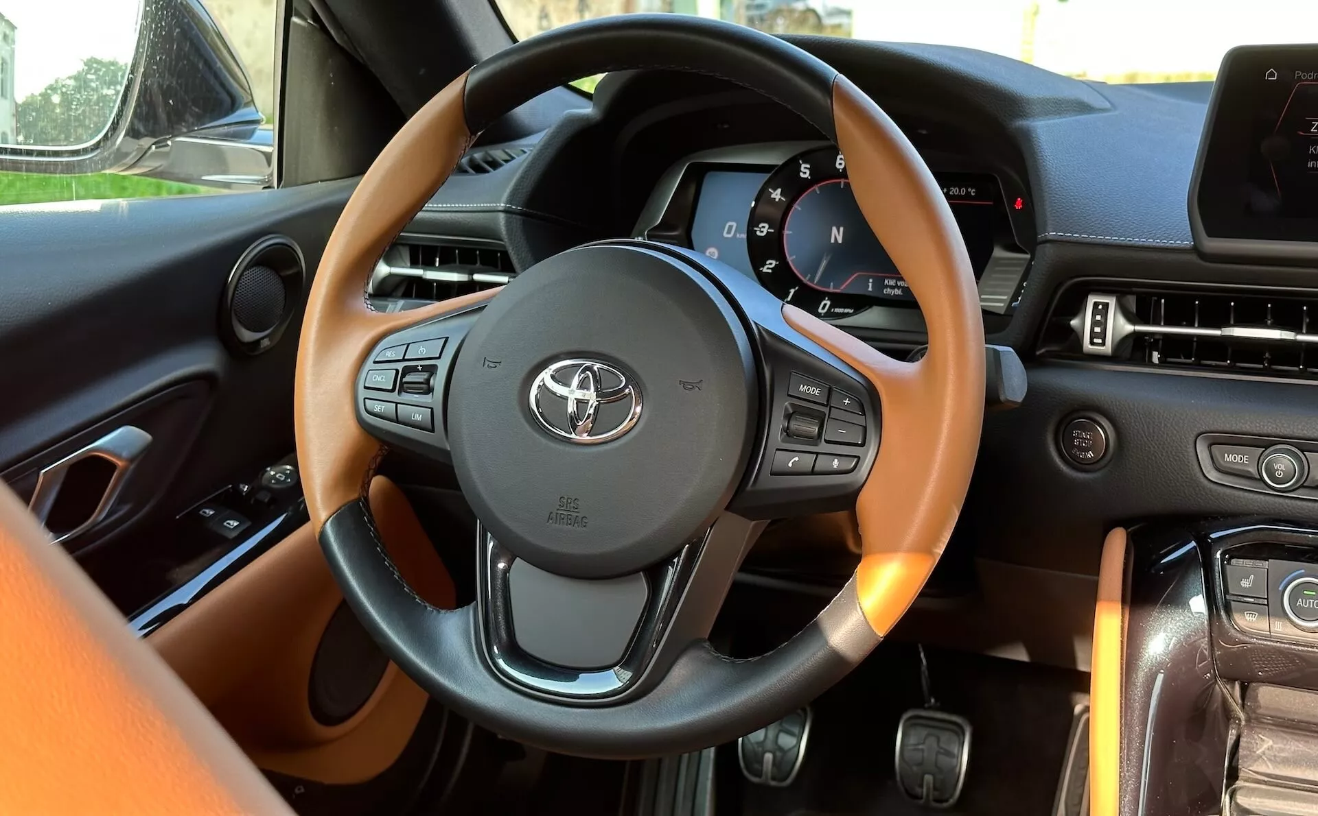 Interiér Toyota Supra (GR-Supra) 2019 z pohledu řidiče s detailním volantem obsahujícím ovládání multimédií a informací o vozidle, digitálním přístrojovým panelem a pokročilým systémem zábavy