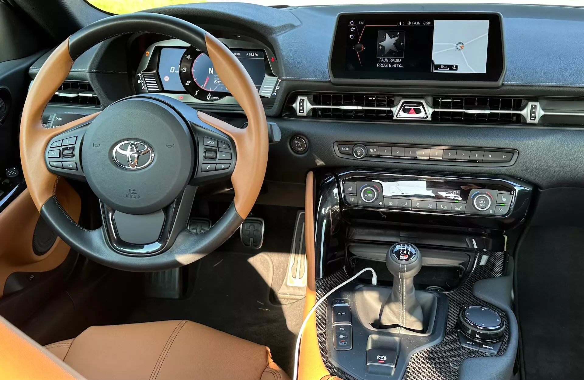 Interiér Toyota Supra GR 2019 představuje centrální multifunkční volant s emblémem Toyota a dřevěnými akcenty, digitální přístrojový panel se speedometrem a otáčkoměrem, dotykový displej infotainmentu s ovládáním klimatizace, automatickou volící páku s ovládáním jízdních režimů a luxusní povrchy z kůže, dřeva a kovu.