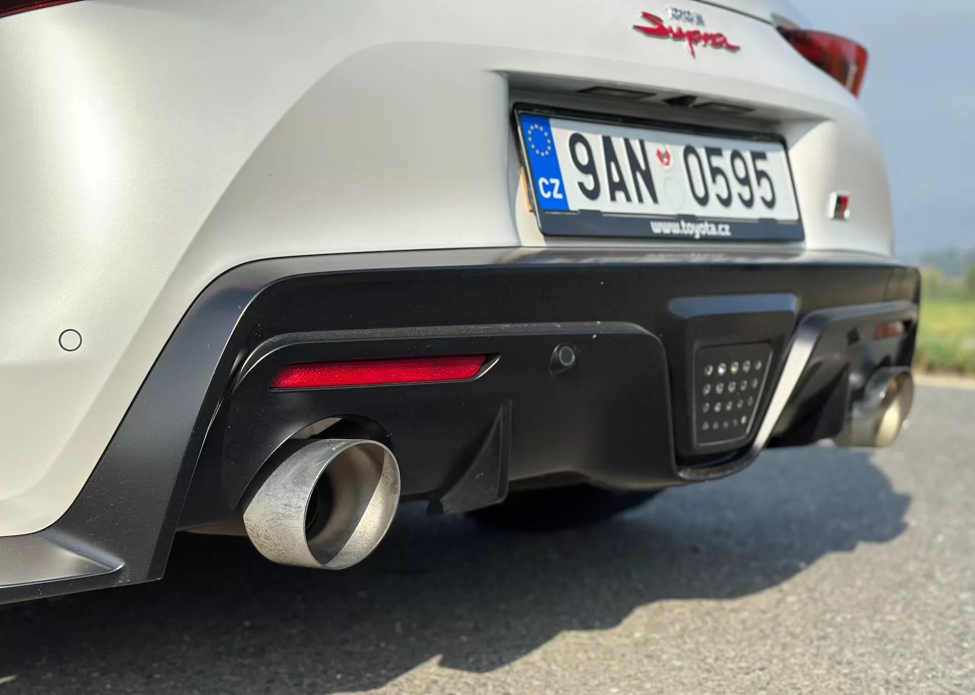 Detailní záběr zadní části Toyoty Supra GR 2019, ukazuje spodní část nárazníku, výfukový systém a pokročilou aerodynamiku, fotografováno z nízkého úhlu, aby byly zdůrazněny vlastnosti výkonu a zaparkováno s poznávací značkou České republiky.
