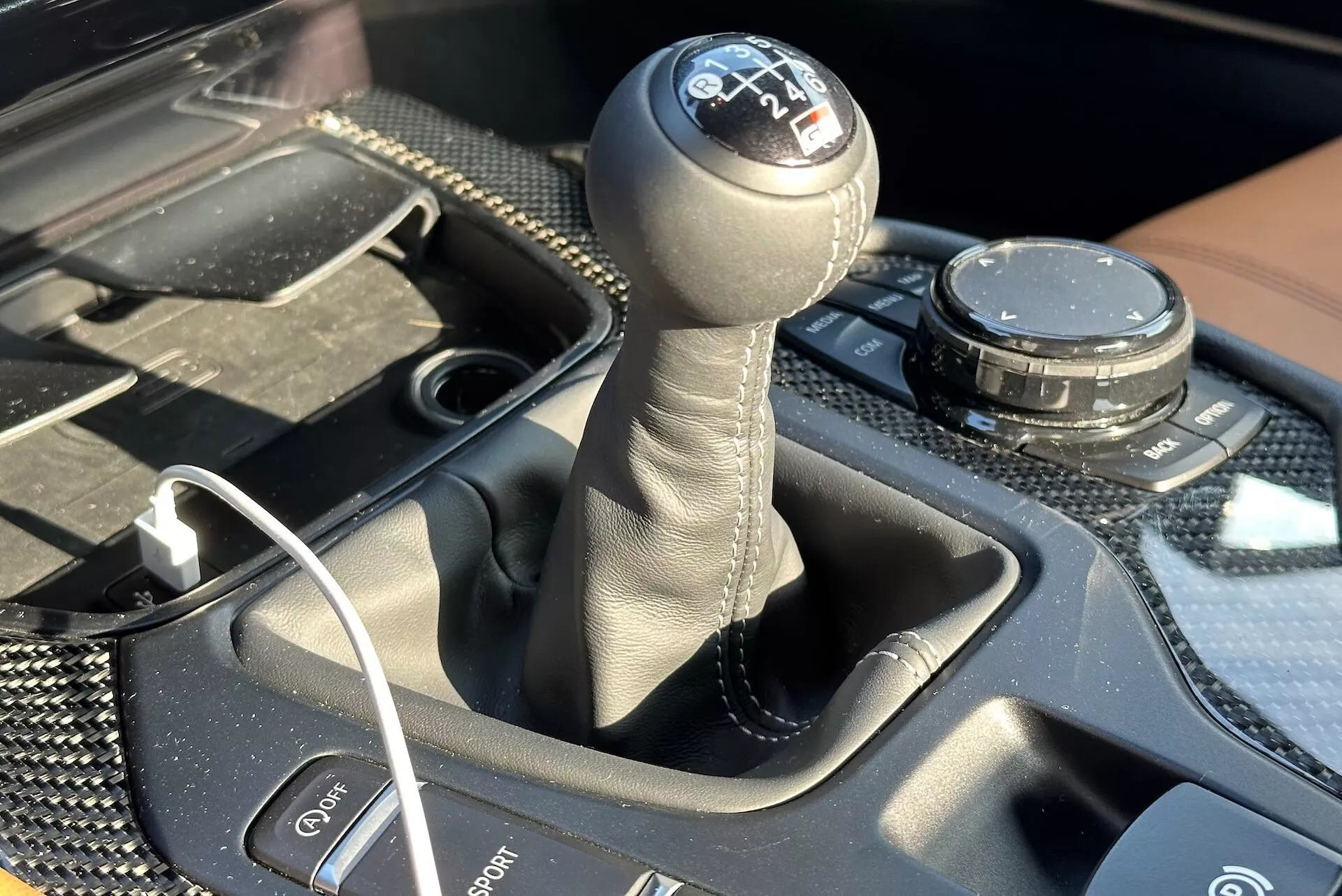 Detailní pohled na manuální řadicí páku Toyoty Supra GR 2019 s 6stupňovým schématem, koženými detaily, konzolí okolo a ovládacím kolečkem multimediálního systému