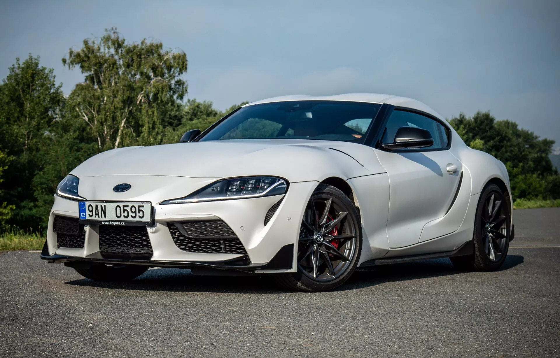 Toyota Supra GR 2019 ve dne, ukazující aerodynamický design, agresivní přední část s velkými vzduchovými vstupy a elegantními světlomety, boční profil s litými koly a brzdami pro vysoký výkon, a kvalitní lakovanou povrchovou úpravou.