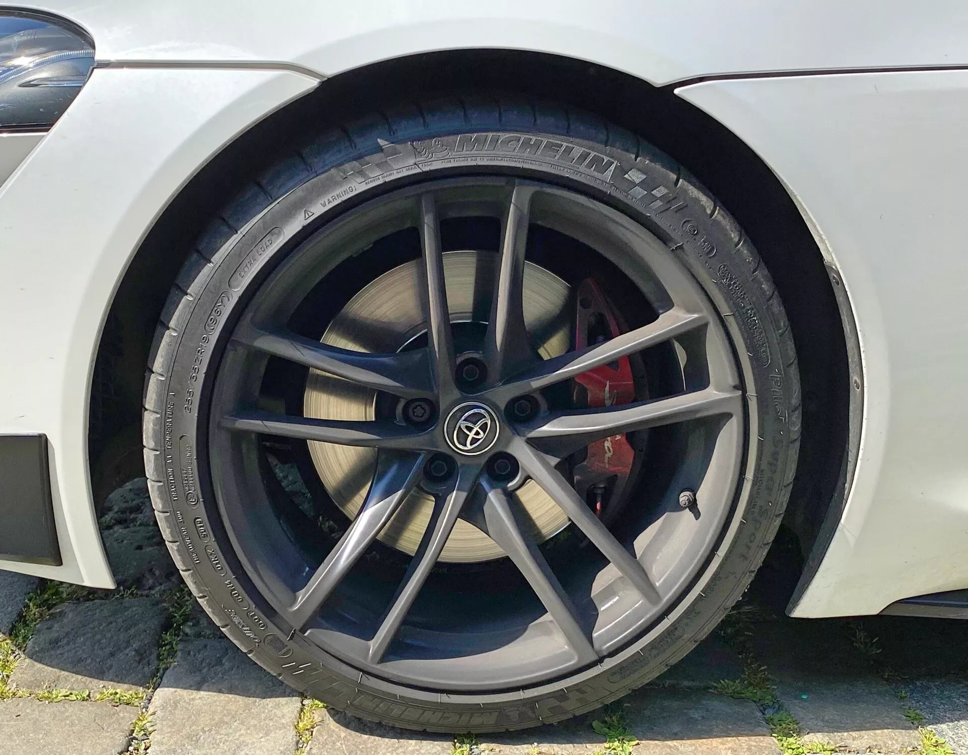 Detailní záběr předního kola automobilu zaměřený na stranu řidiče s černým pětipaprskovým litým ráfkem, červeným brzdovým třmenem a pneumatikou značky Pirelli, což naznačuje sportovní a výkonný vzhled.