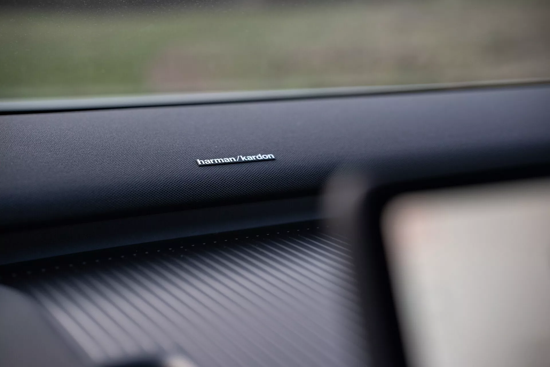 Interiérový snímek Volvo EX30 rok 2024 se zaměřením na značení audio systému Harman/Kardon na palubní desce na straně spolujezdce, který prezentuje materiál vysoké kvality a zdůrazňuje přední technologii zvukového systému.