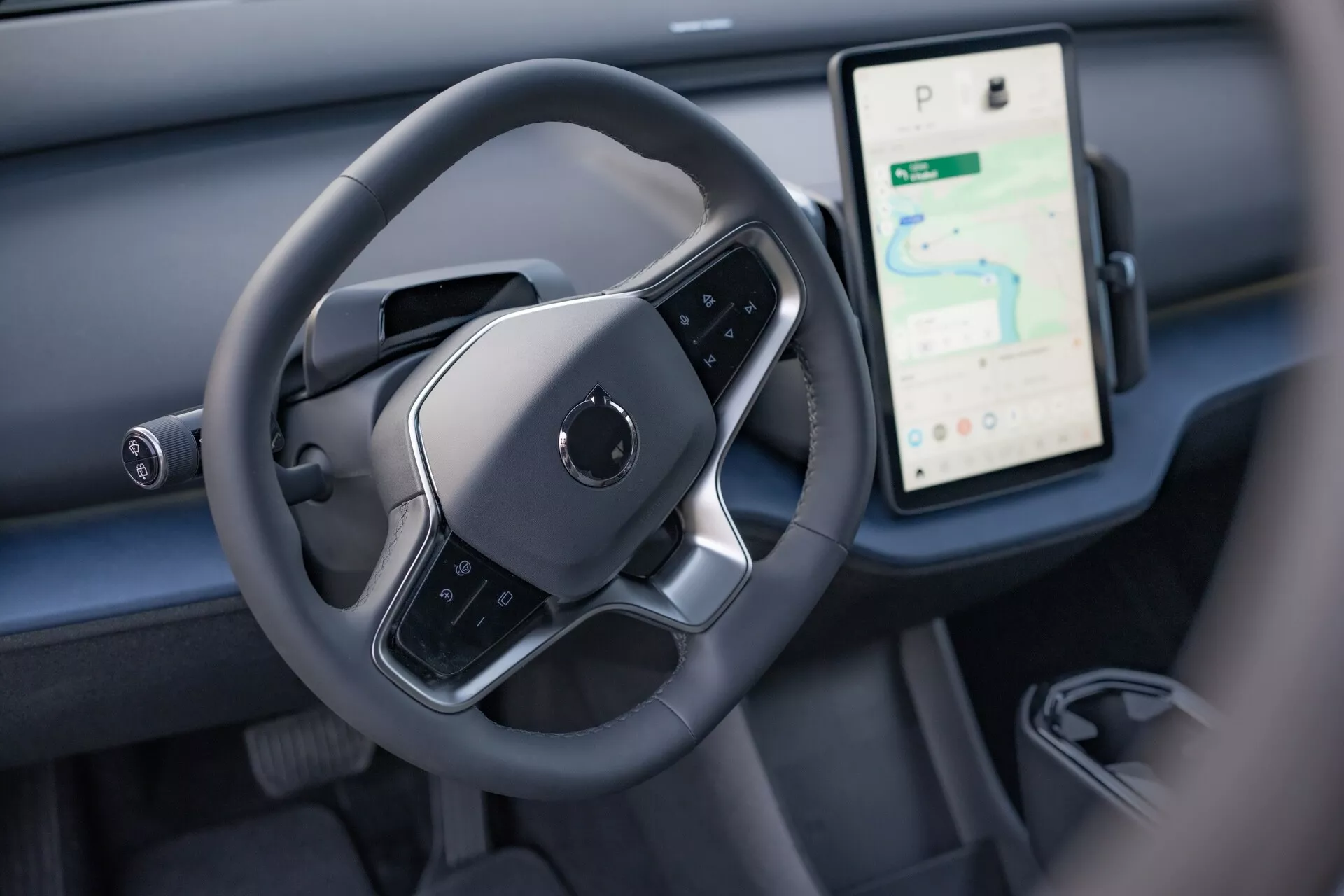 Interiér Volvo EX30 2024 s výhledem na prostor řízení řidiče s moderním volantem s plochým dnem a velkým vertikálním dotykovým displejem pro navigaci a média na palubní desce