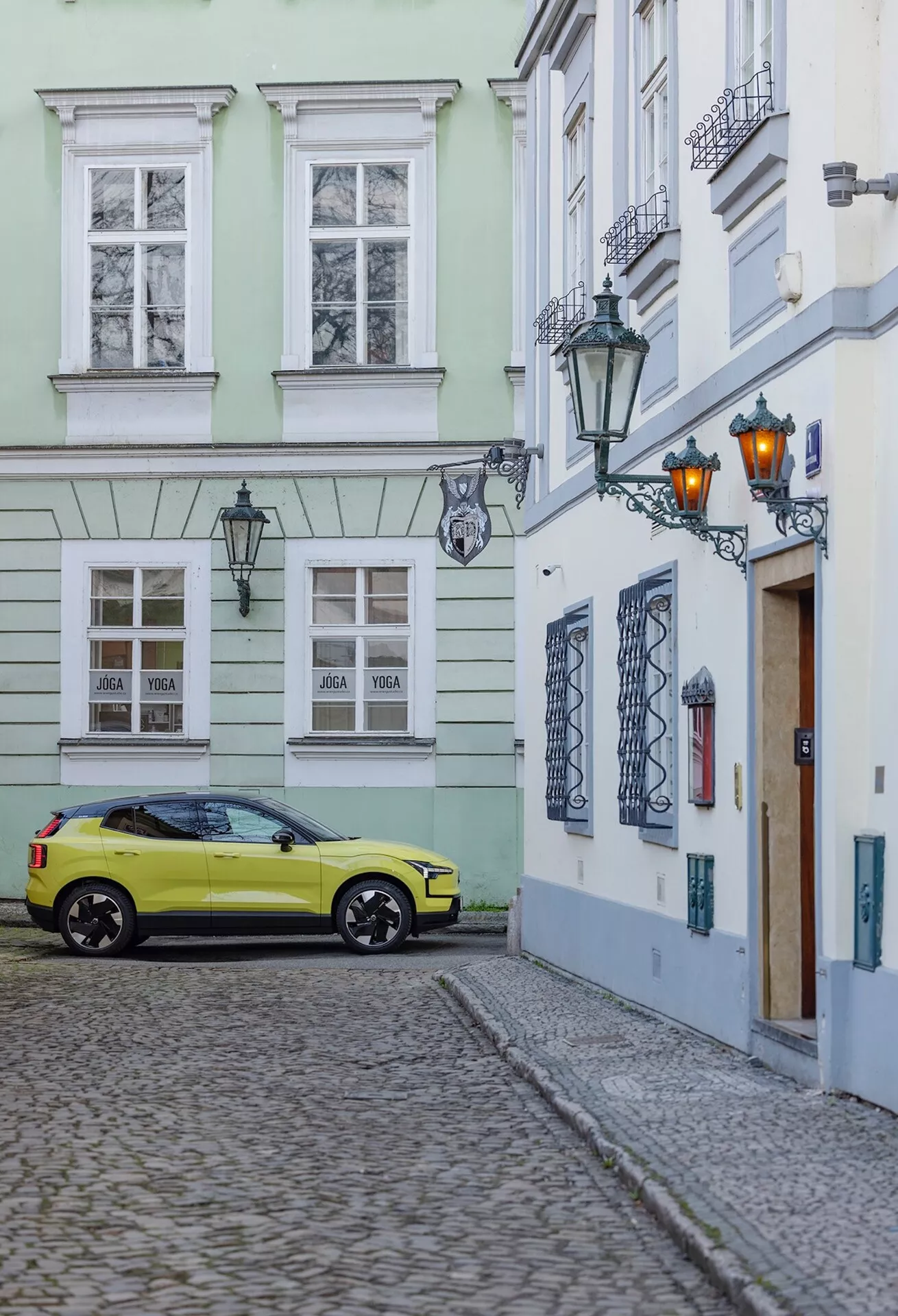 Volvo EX30 2024 zaparkované na dlážděné ulici v historickém prostředí, zachycené ze tříčtvrtečního zadního úhlu, který ukazuje pravou stranu a zadní část vozu včetně kol, zadních světel a částečných detailů střechy ve výrazné žluté barvě