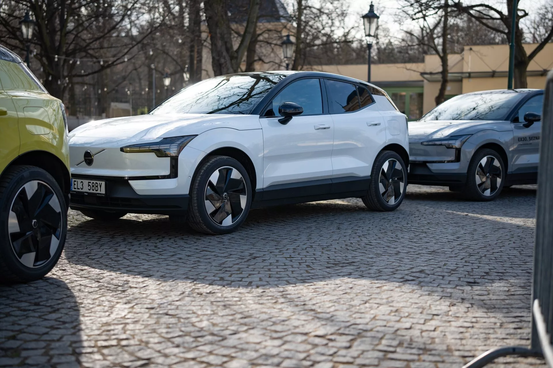 Bílé moderní crossover SUV roku 2024 ve tříčtvrtečním pohledu zaparkované na dlažební ulici, s lesklým lakem, LED denními světly, zapuštěnými klikami dveří a dynamicky navrženými slitinovými koly naznačujícími luxus a výkon, pravděpodobně elektrické vozidlo.