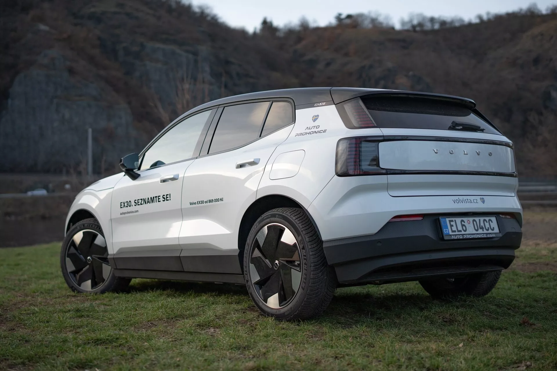 Zadní tříčtvrteční pohled na elektrický crossover Volvo EX30 rok 2024 v bílé barvě, zdůrazňující jeho moderní design, slitinová kola, parkovací senzory a funkce asistence řidiče