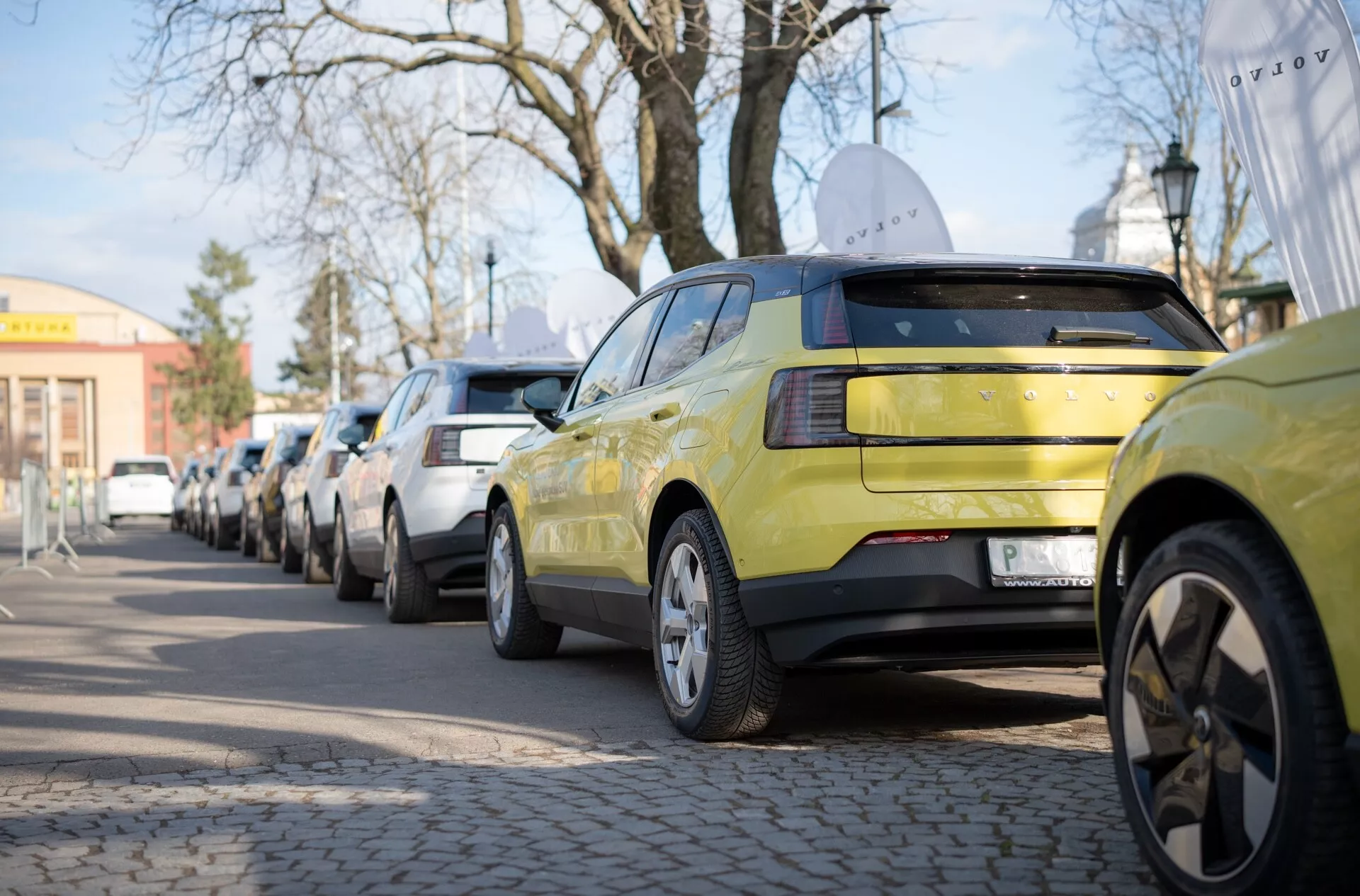 Lindově zelený Volvo EX30 z roku 2024, který předvádí jeho zadní část s LED světly a litými ráfky, parkovaný podél městské ulice