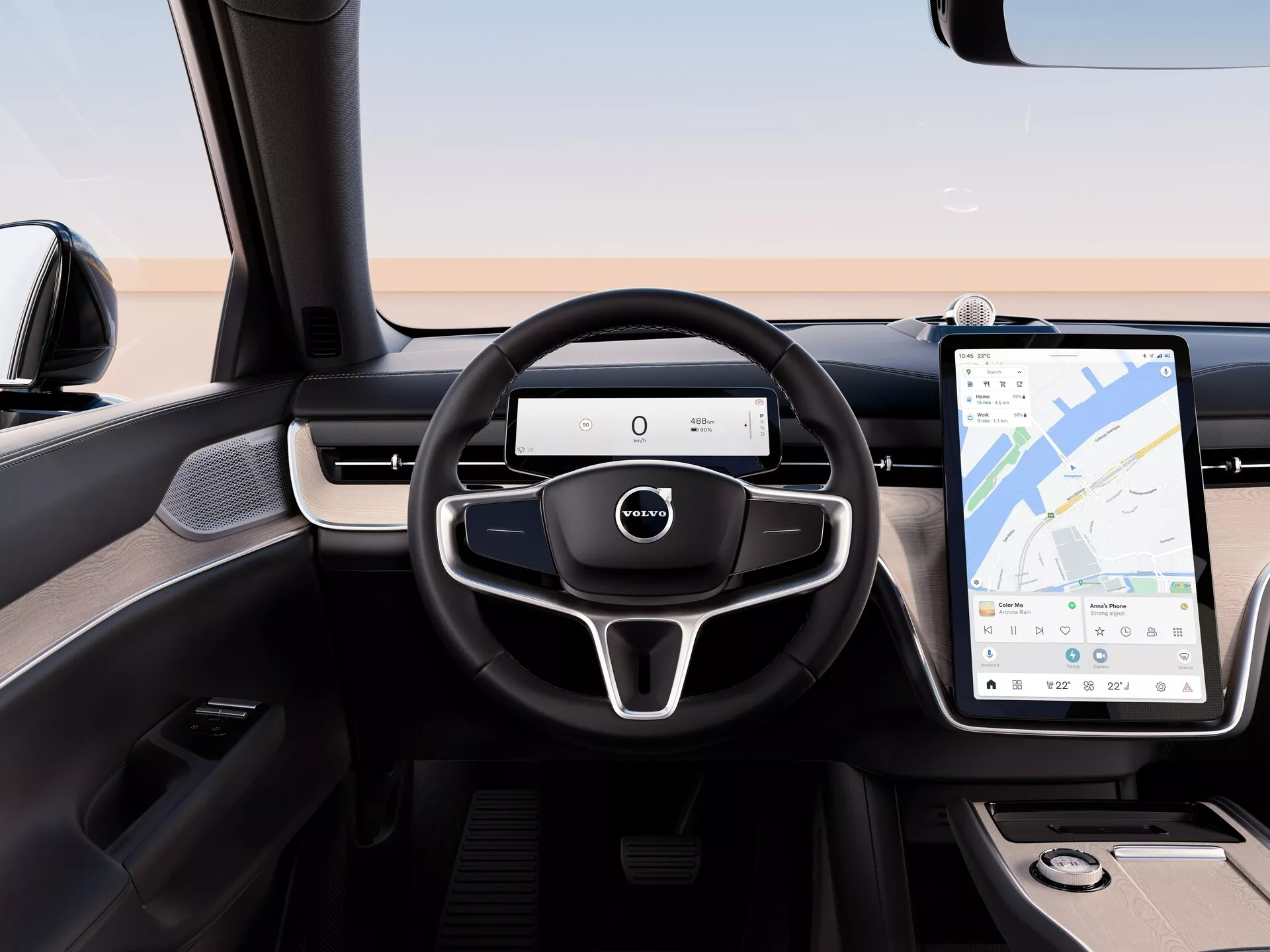 Interiér Volvo EX90 2023 z pohledu ze zadního sedadla, zdůrazňující moderní volant se třemi paprsky s multifunkčními ovladači, digitální přístrojový panel a velký dotykový informační systém s navigací GPS