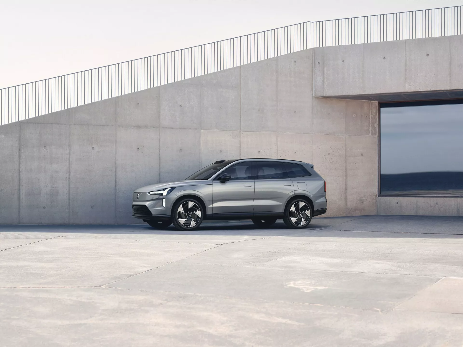 Volvo EX90 1. generace z roku 2023 zaparkované venku, pohled z boku předvádí úhlový design, zapuštěné kličky dveří a slitinová kola na pozadí minimalistické architektury