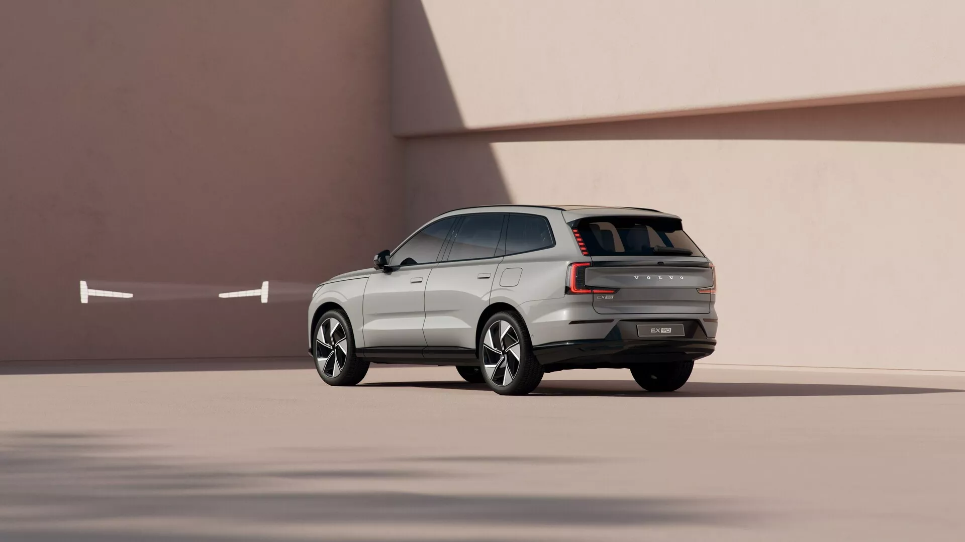 SUV Volvo EX90 2023 v dynamické bočně-zadní perspektivě na pozadí s hladkou minimalistickou texturou, předvádějící designové linie, modelovaná litá kola a pokročilé technologické funkce.