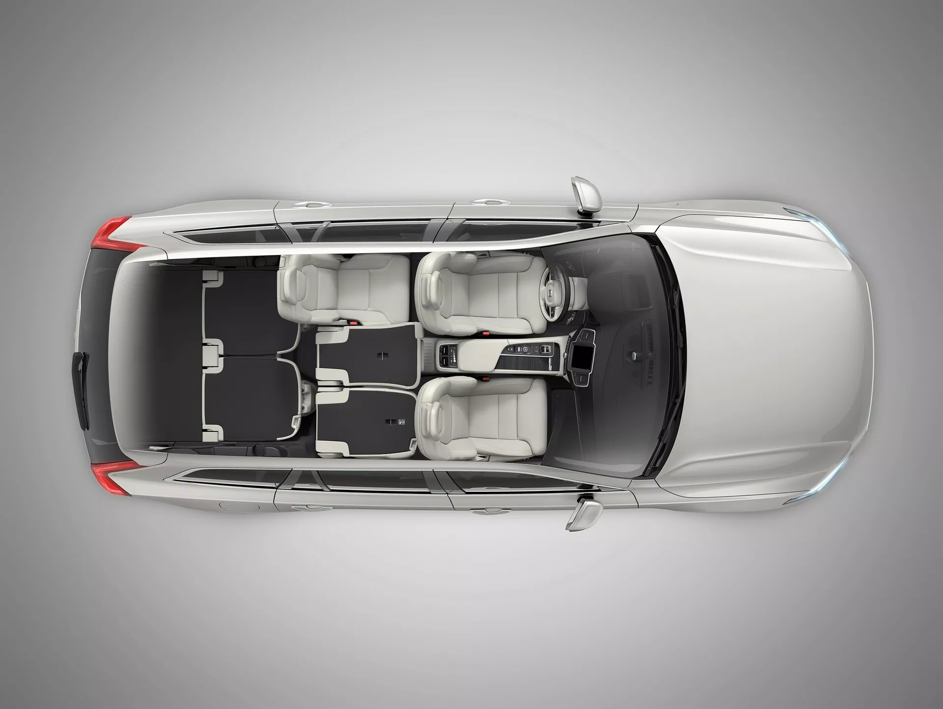 Pohled z ptačí perspektivy na sedan Volvo XC90 druhé generace z roku 2015 s průhlednou nebo digitálně odstraněnou střechou, který odhaluje interiér. Obrázek ukazuje dlouhou kapotu, čtyři zavřené dveře, čtyři kola a uspořádání sedadel se dvěma předními sedadly a zadní lavicí pro tři cestující. Viditelná středová konzole a řadicí páka. Zobrazeno uspořádání levého řízení s volantem, displejem a ovládacími prvky na palubní desce. Jsou patrné konstrukční prvky jako opěrky hlavy, vnější zrcátka a celkový vnitřní prostor a uspořádání.